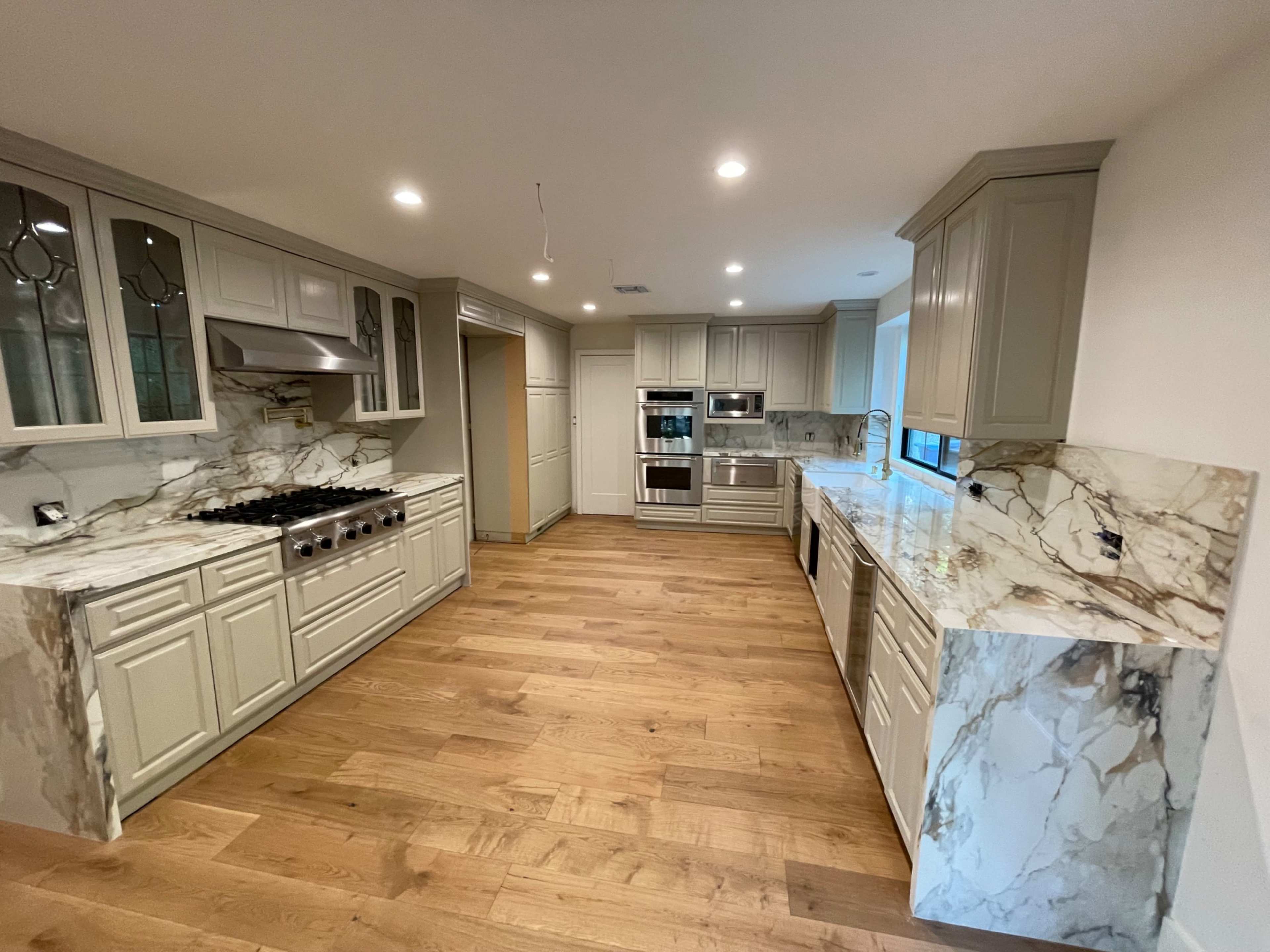 The image shows a modern kitchen featuring light-colored cabinets, marble countertops, and stainless steel appliances.