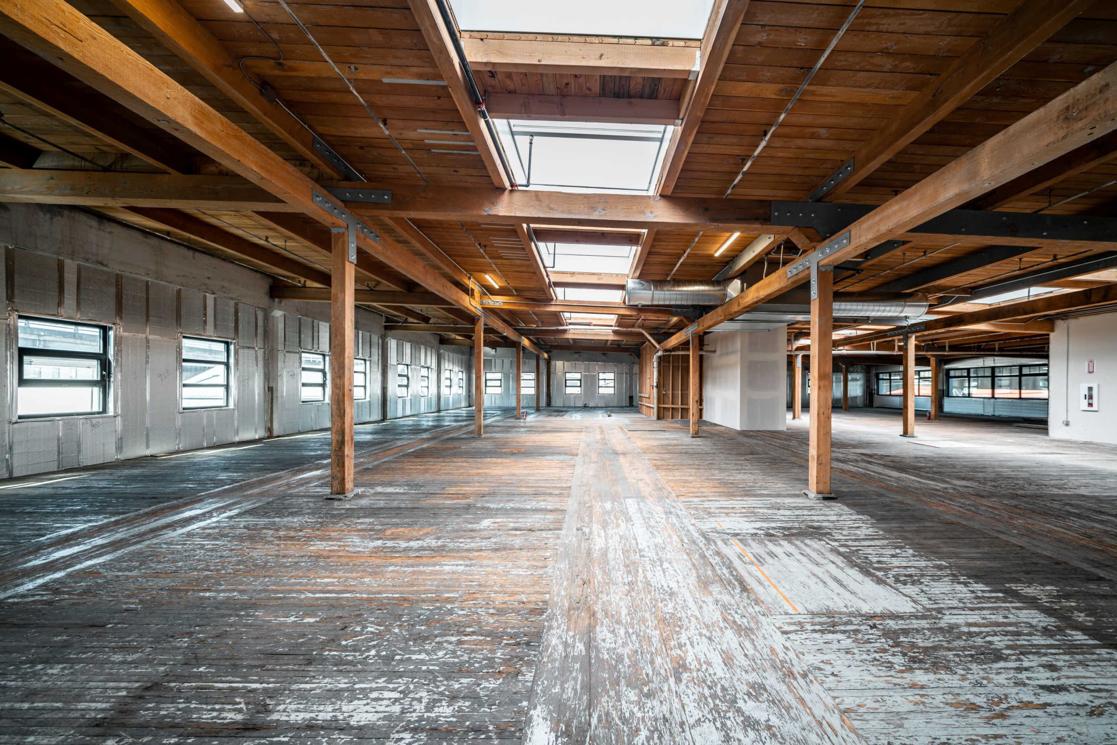 The image shows a spacious interior of a renovated industrial building with wooden beams and large windows.