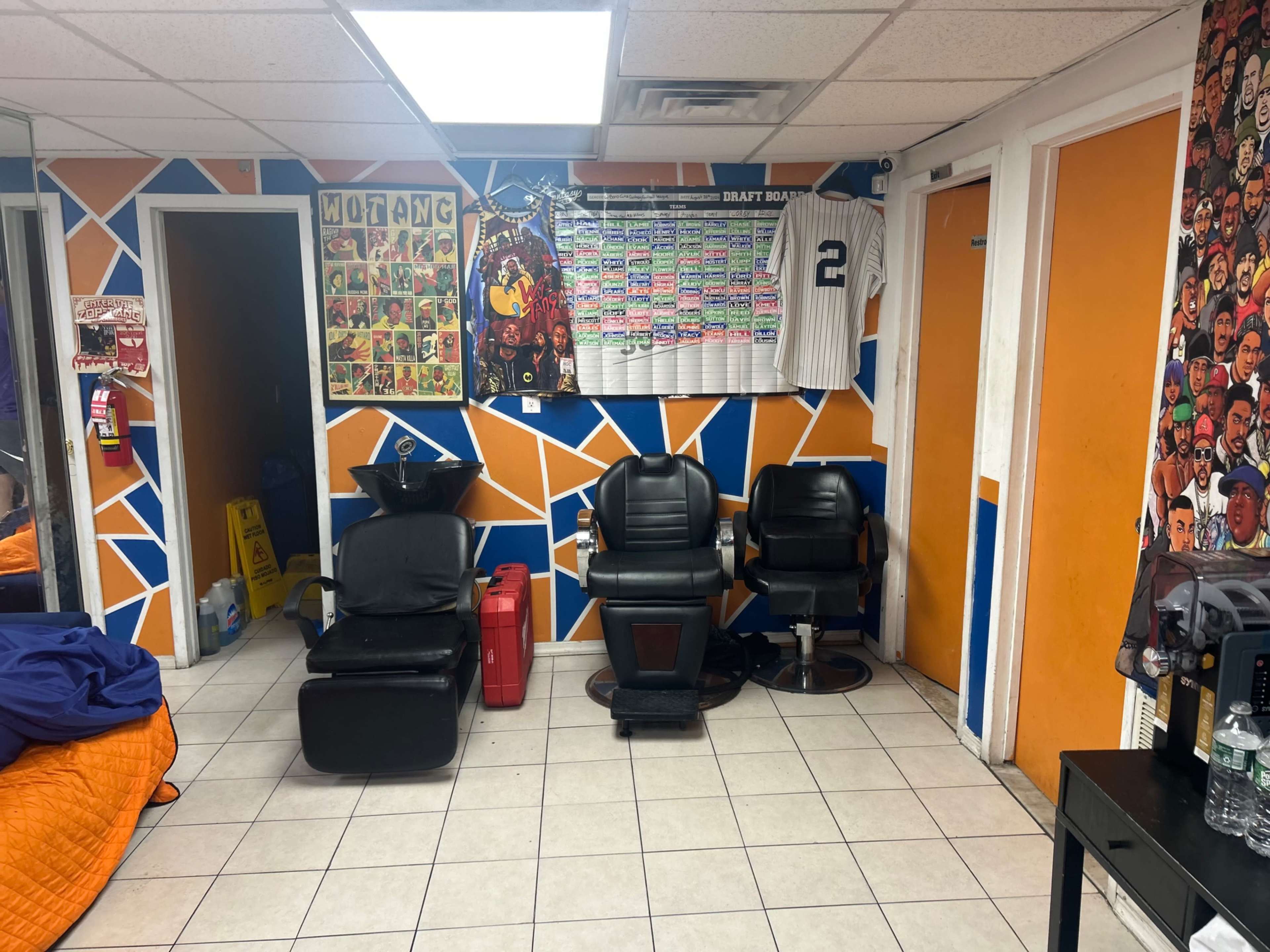 The image shows a barbershop interior with two black barber chairs, colorful wall decorations, and a display of sports memorabilia.