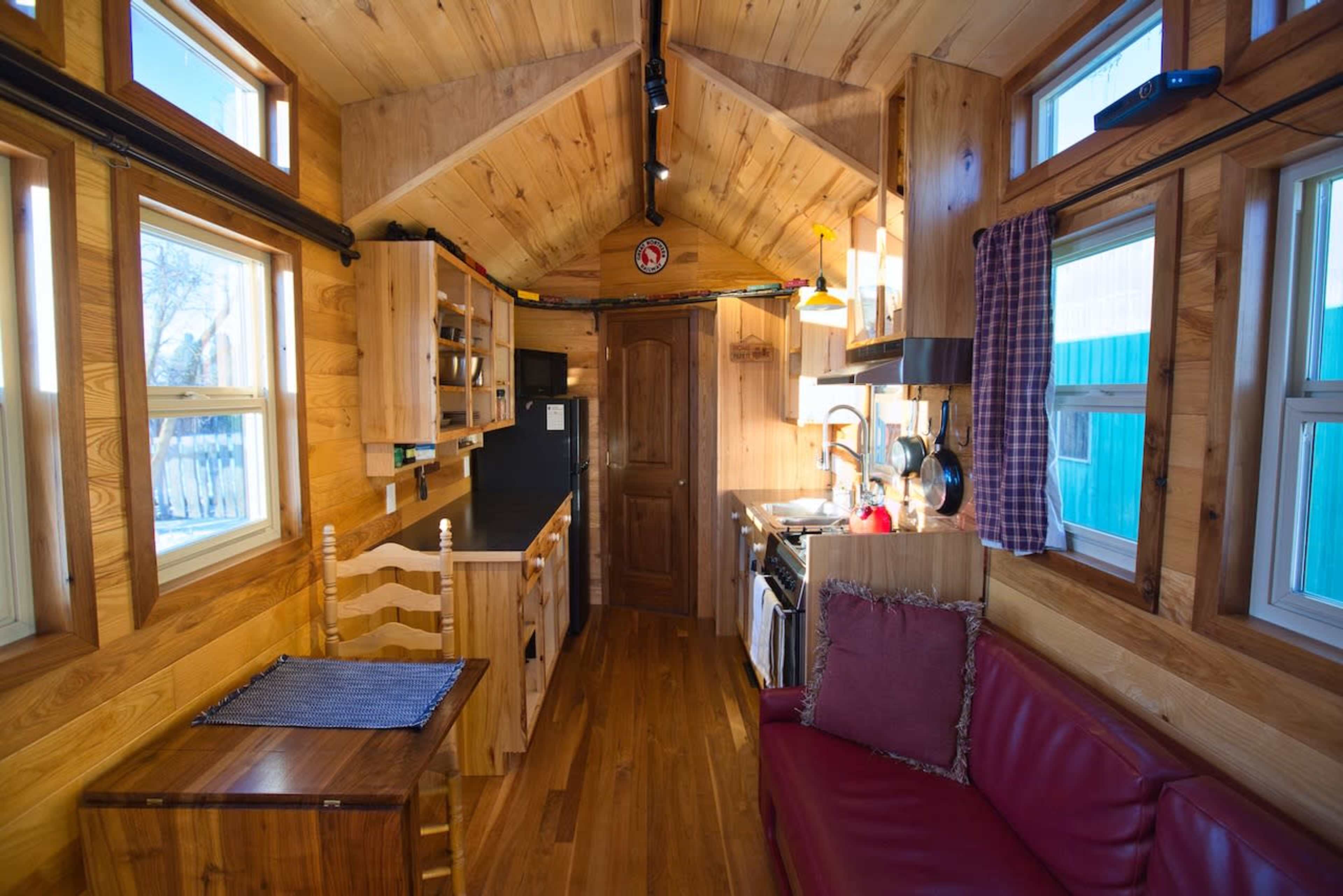 The interior of a small wooden cabin featuring a kitchen area, a dining table, and a red couch.