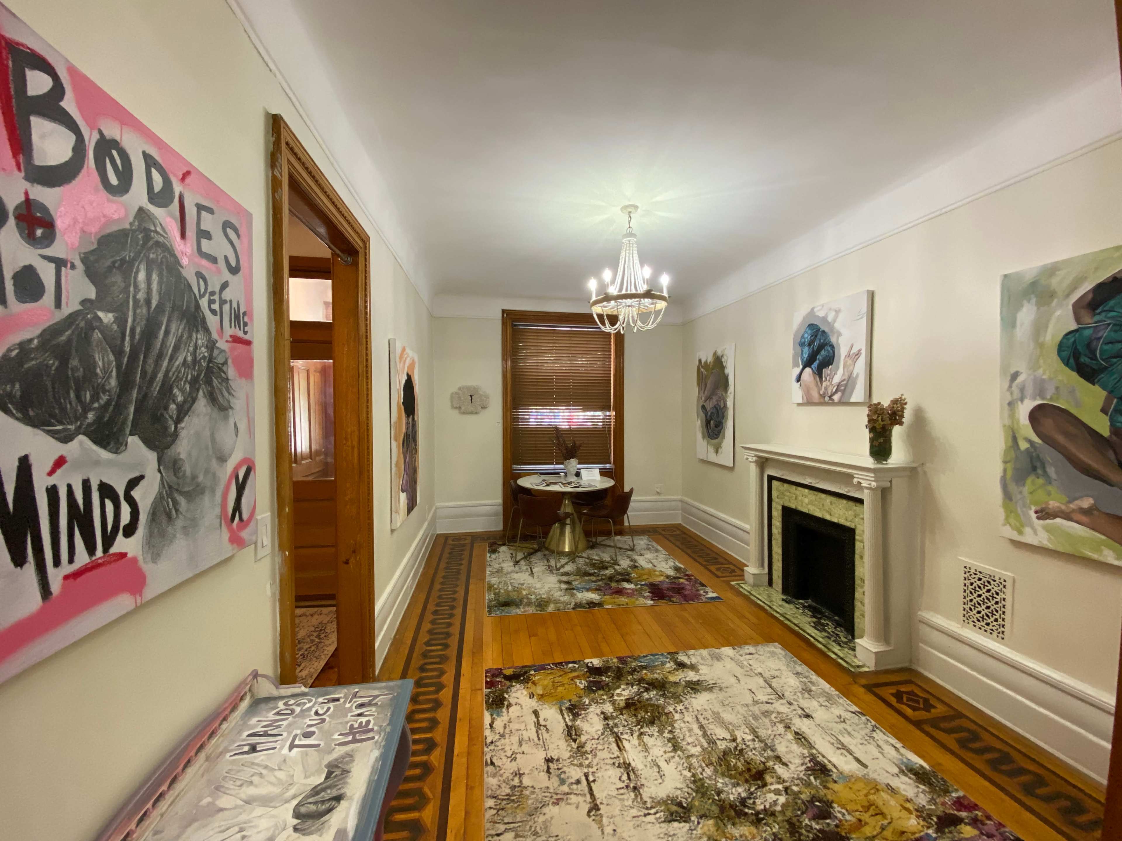 A well-lit hallway features artwork on the walls, a small table with a vase, and a fireplace.