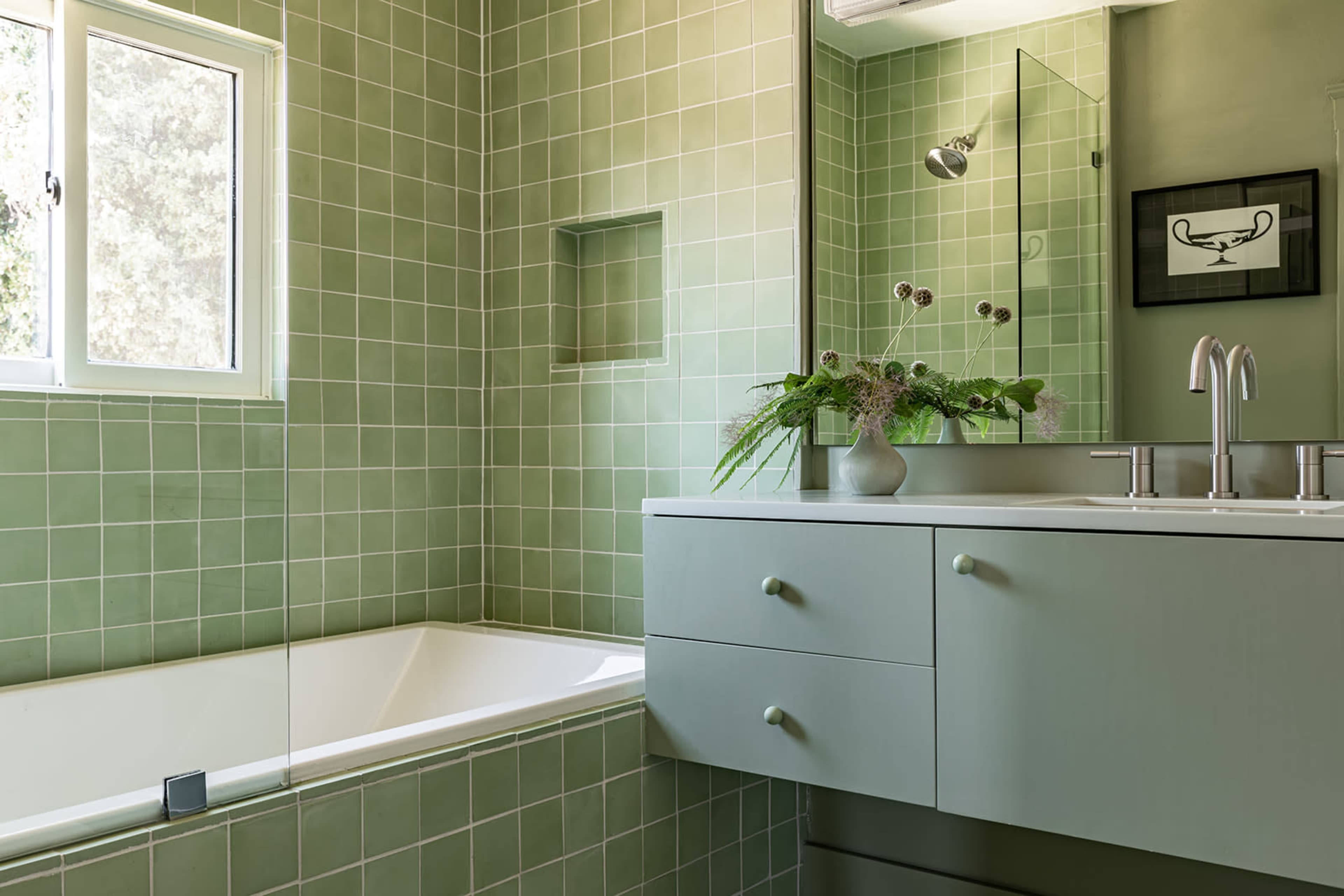 A bathroom featuring green tiles, a bathtub, a modern sink with drawers, and a mirror above the sink.