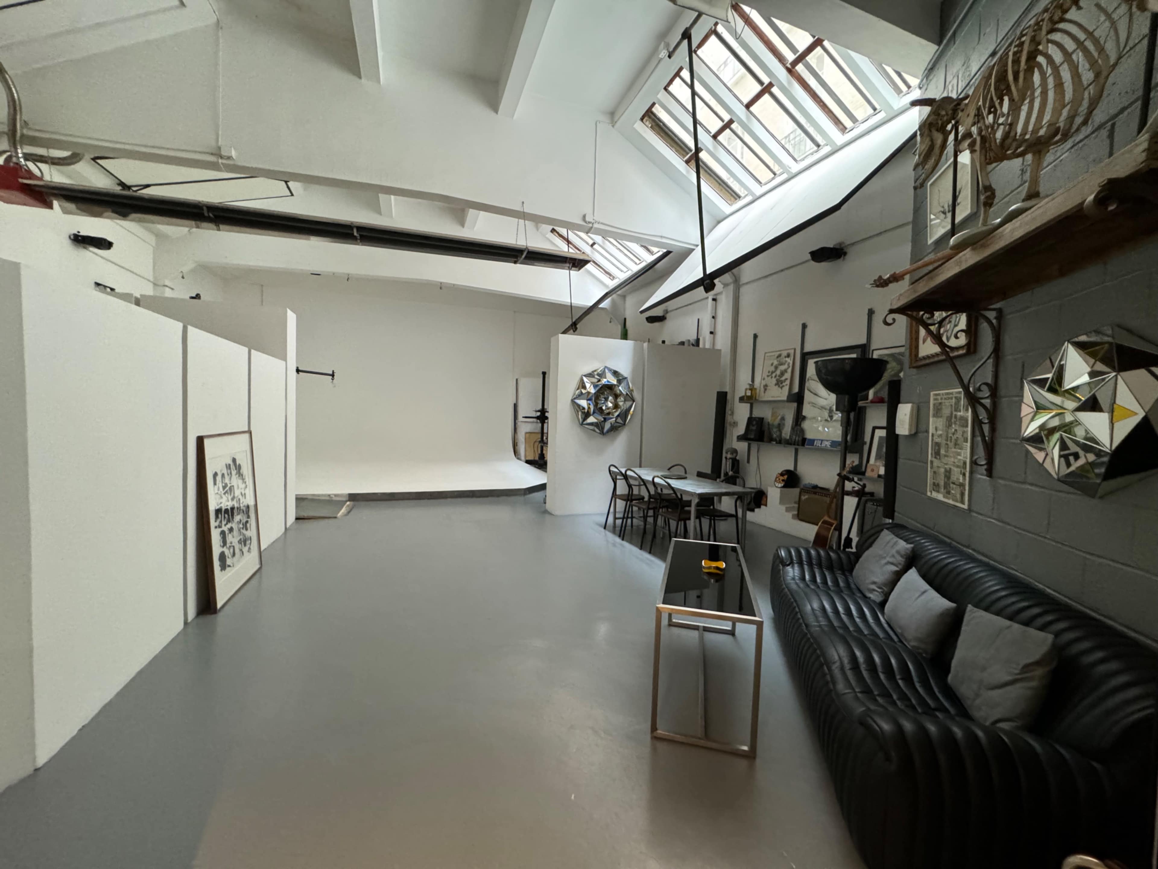 The image shows an artist studio featuring a large open space with white walls, a seating area with a black couch, and various art-related items placed on shelves.