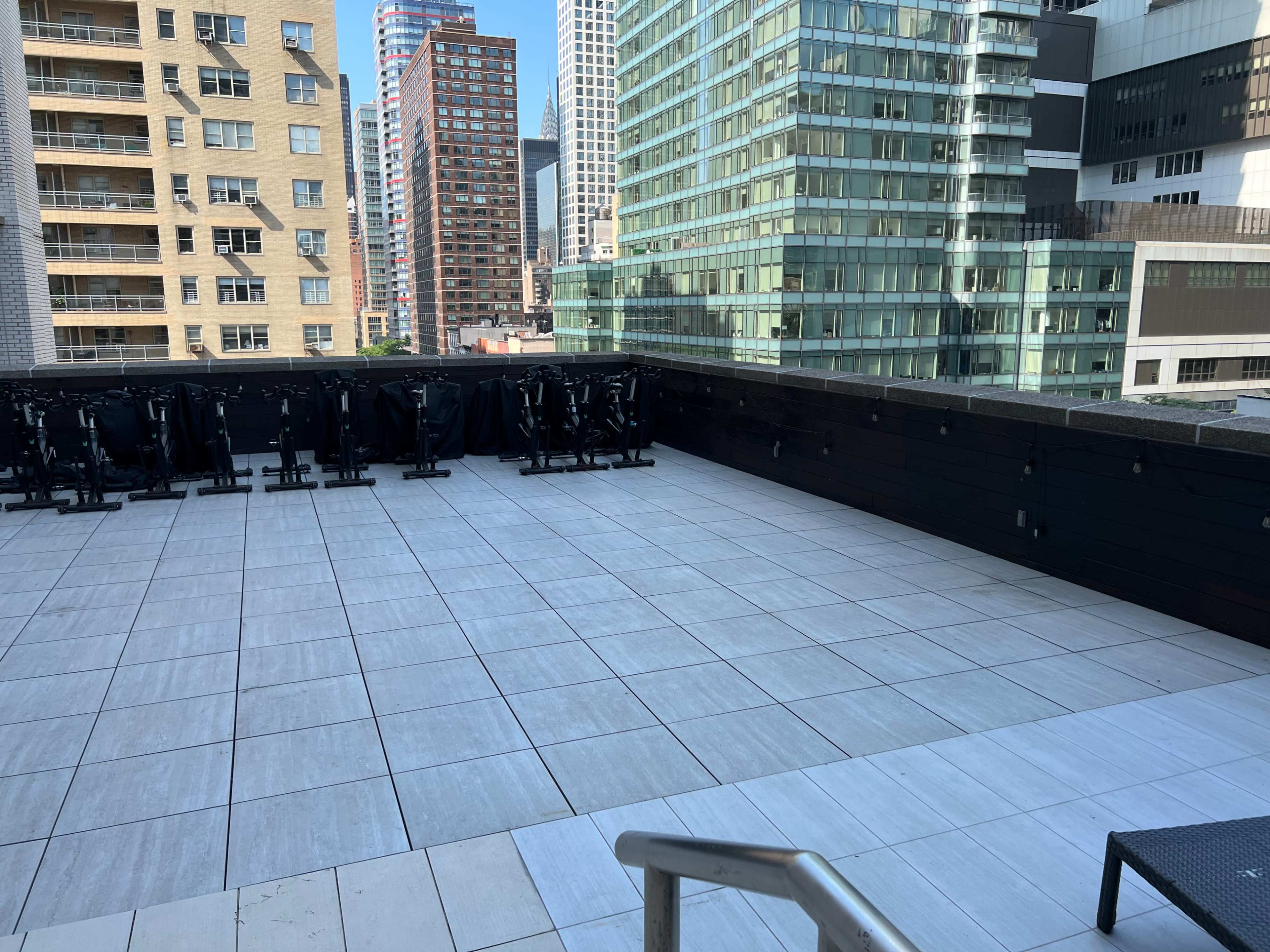 The image shows a rooftop area with gray tiled flooring and several stacked chairs against the backdrop of high-rise buildings.