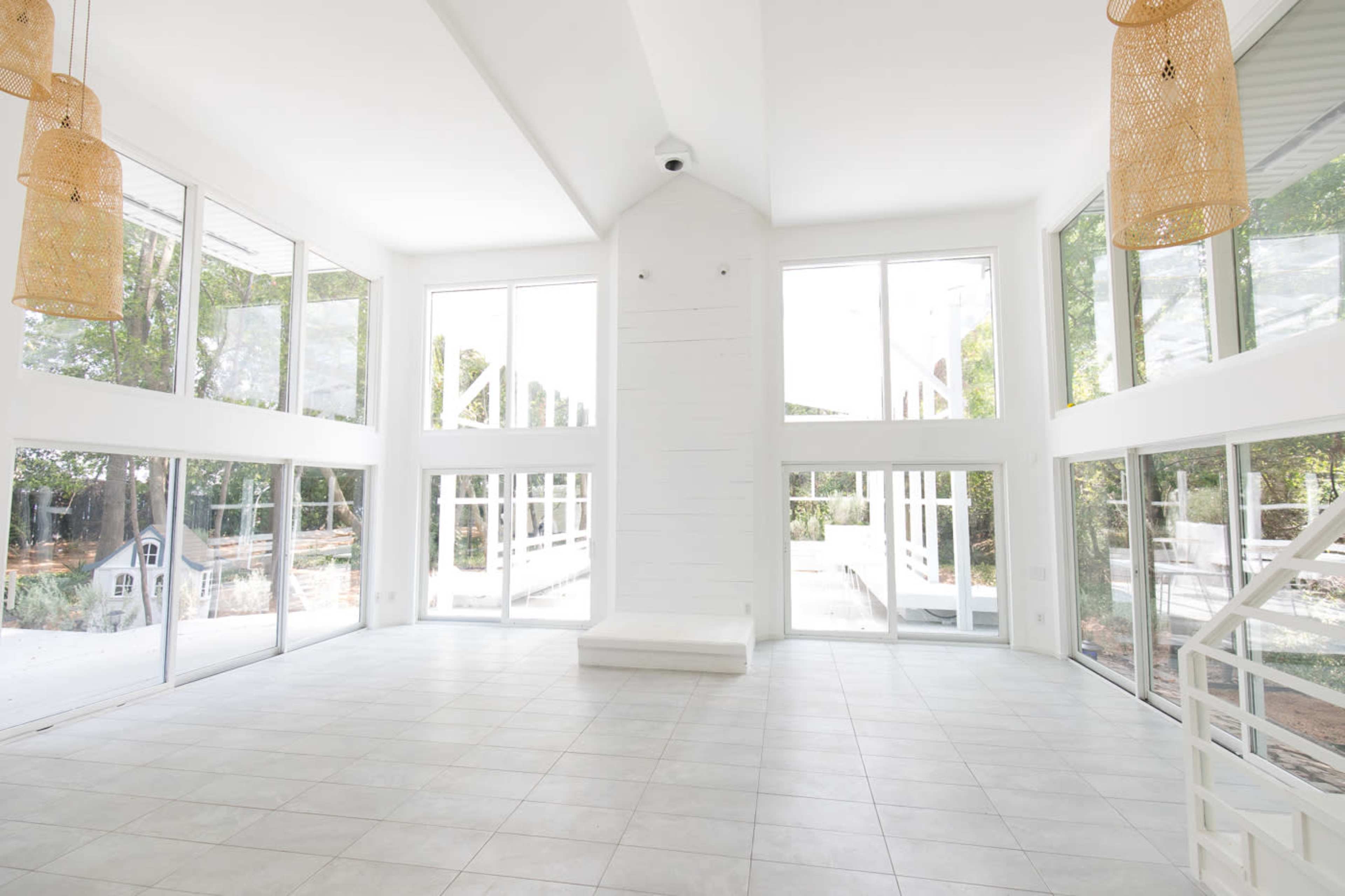 A spacious room with large windows, a high ceiling, and white walls, featuring pendant lights and a tiled floor.