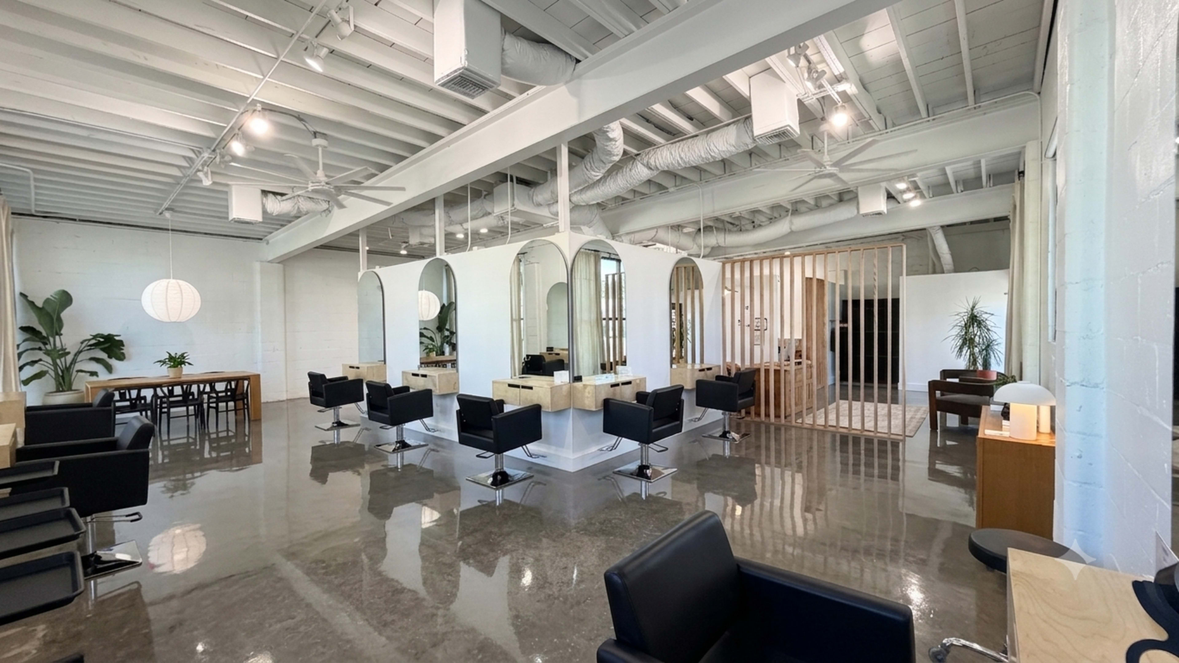 The image shows a modern salon interior with sleek styling stations, mirrors, and a minimalistic design.