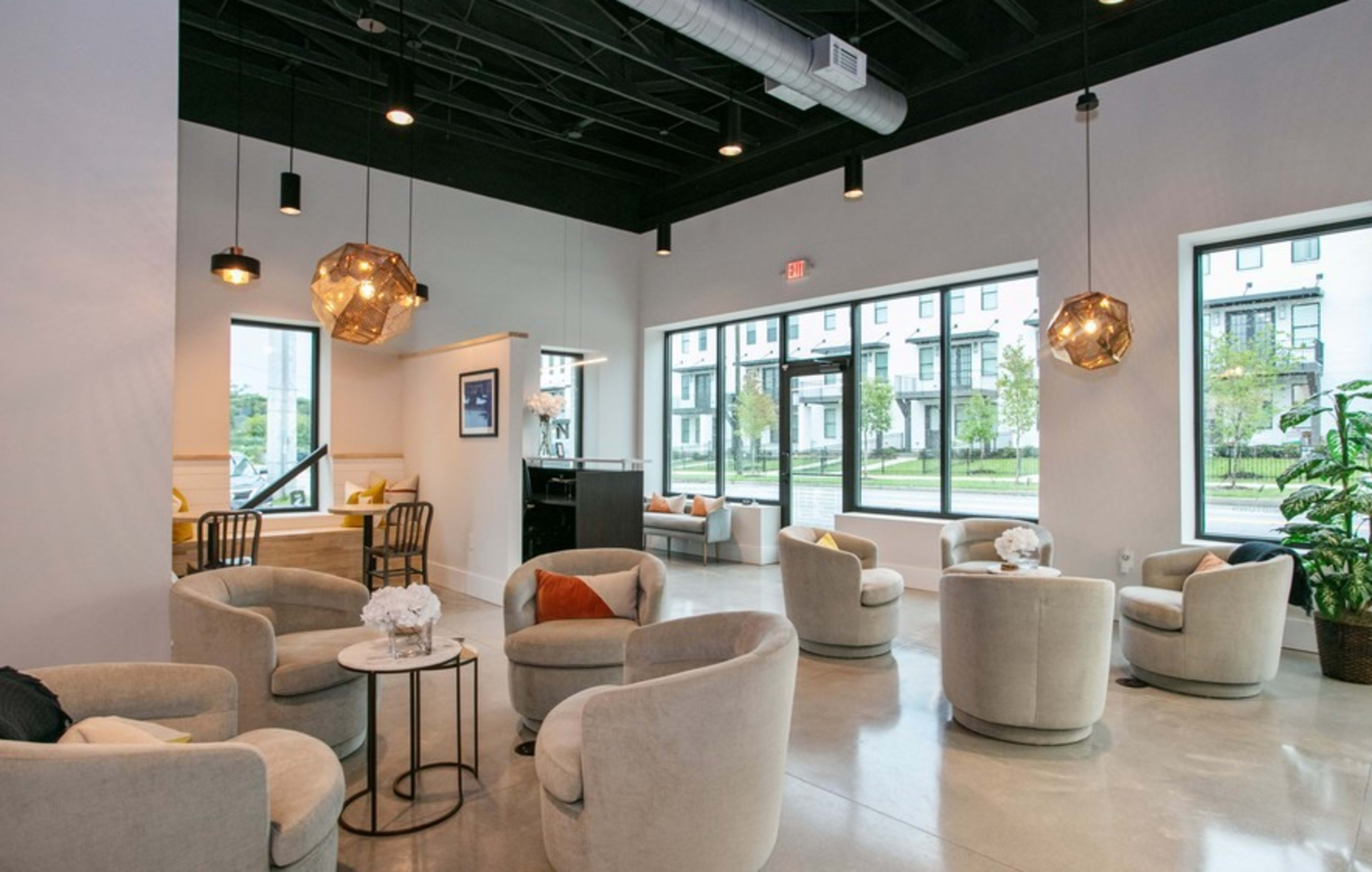 A modern, well-lit lounge area with circular chairs, small tables, and large windows overlooking a streetscape.