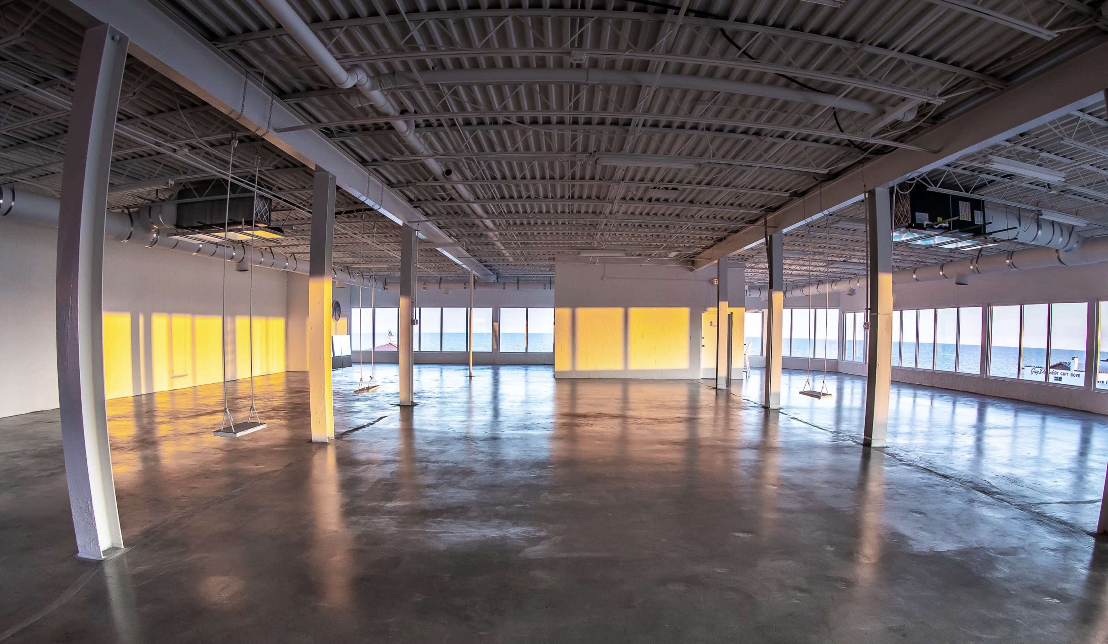 The image shows a spacious, empty interior of a modern building with large windows that let in natural light.