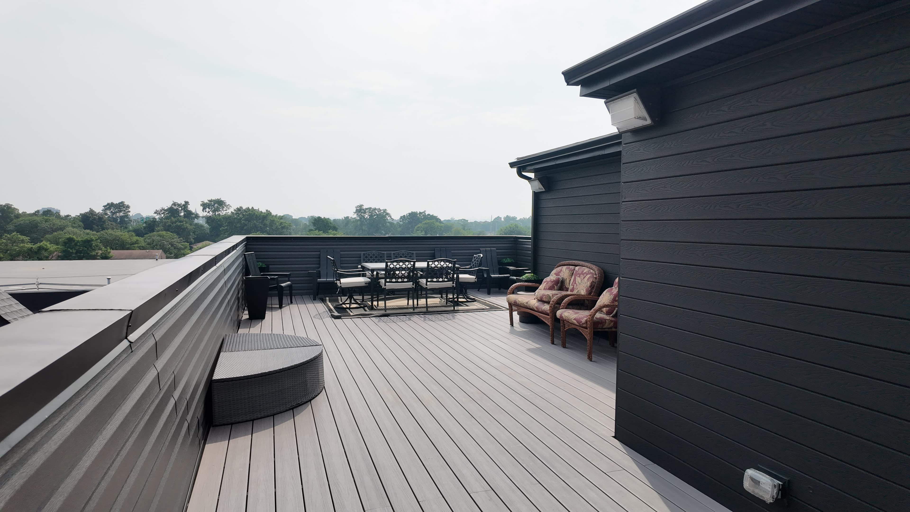 The image shows a spacious rooftop deck featuring outdoor furniture and views of greenery in the background.