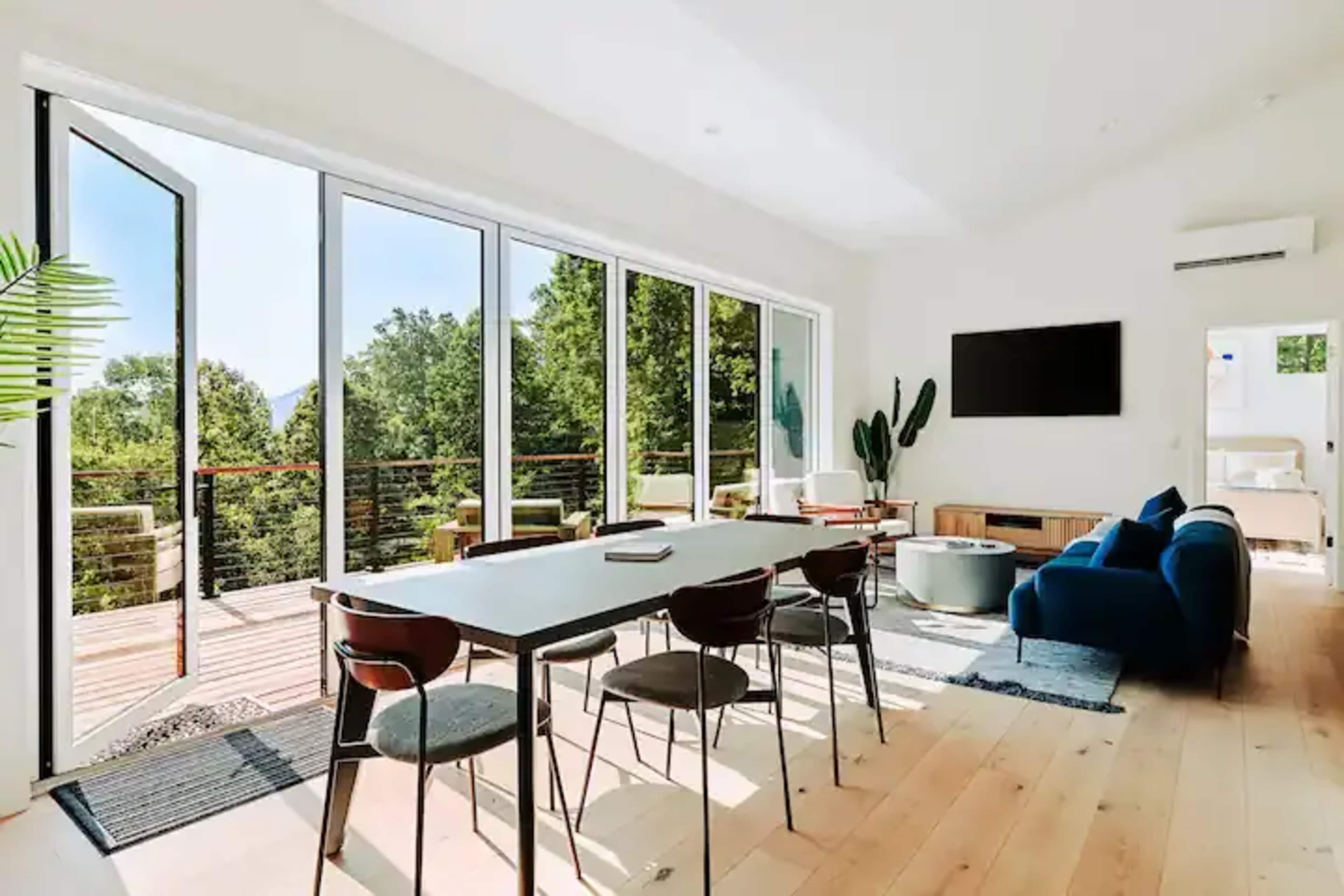 A contemporary living space with large glass doors opening to a deck, furnished with a dining table, chairs, and a blue sofa.