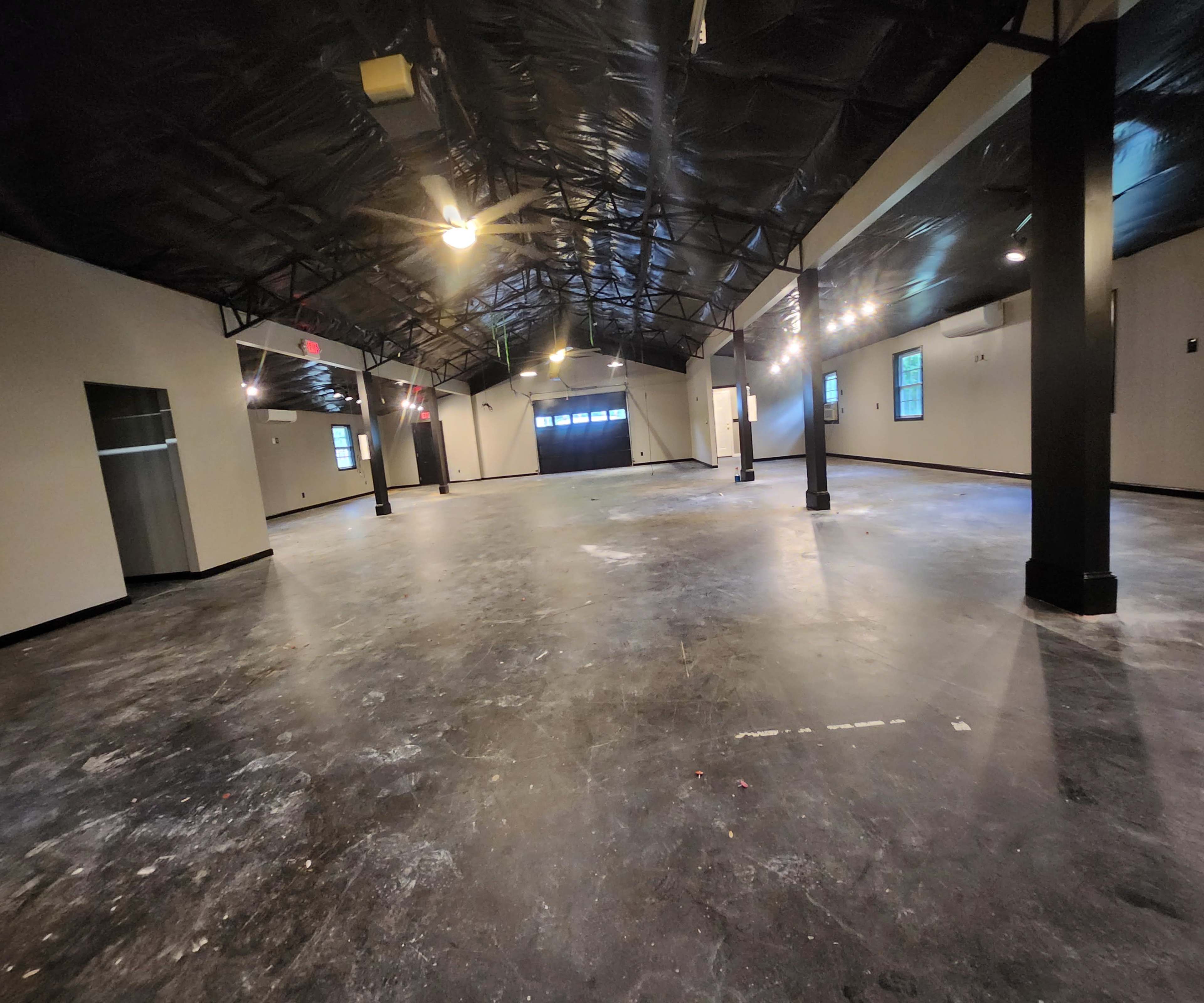 A large, open commercial space with a black ceiling, polished concrete floors, and several light fixtures illuminating the area.