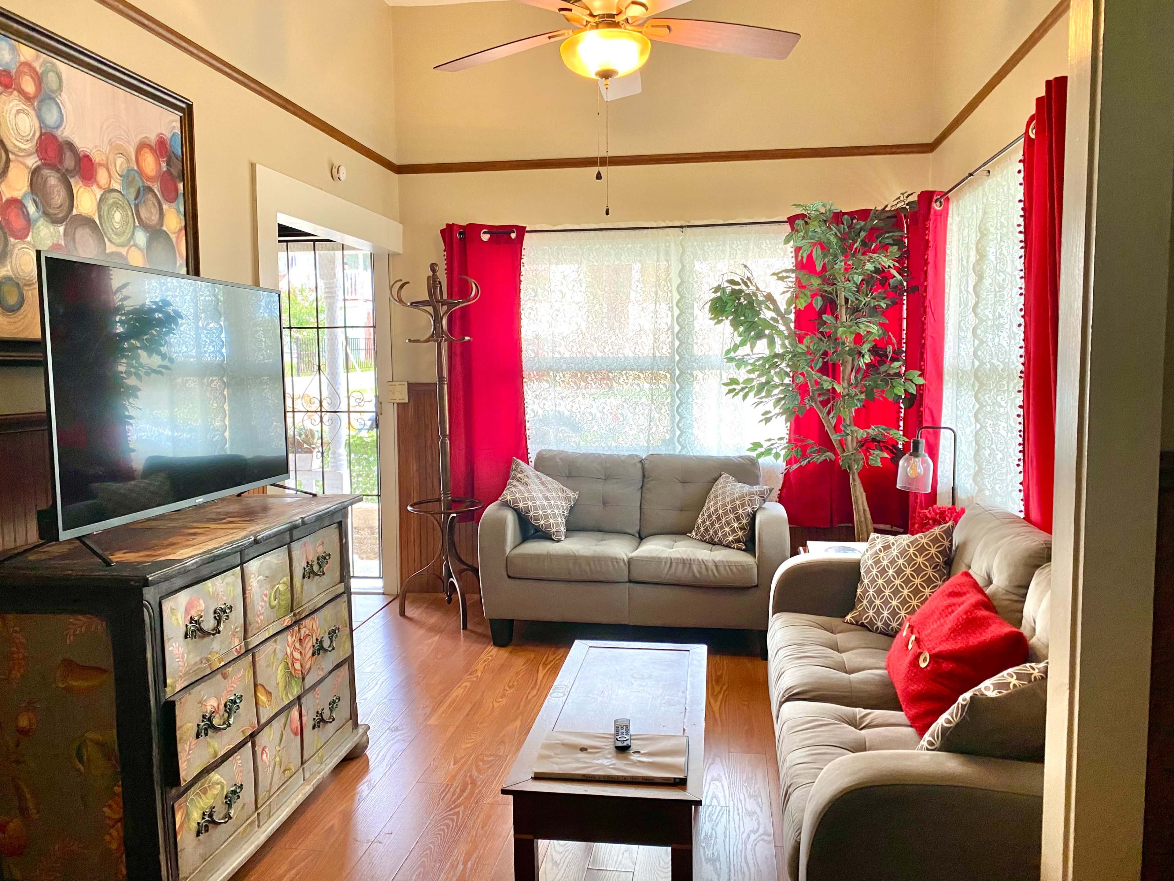A cozy living room with two sofas, a coffee table, a television, and large windows adorned with red curtains.