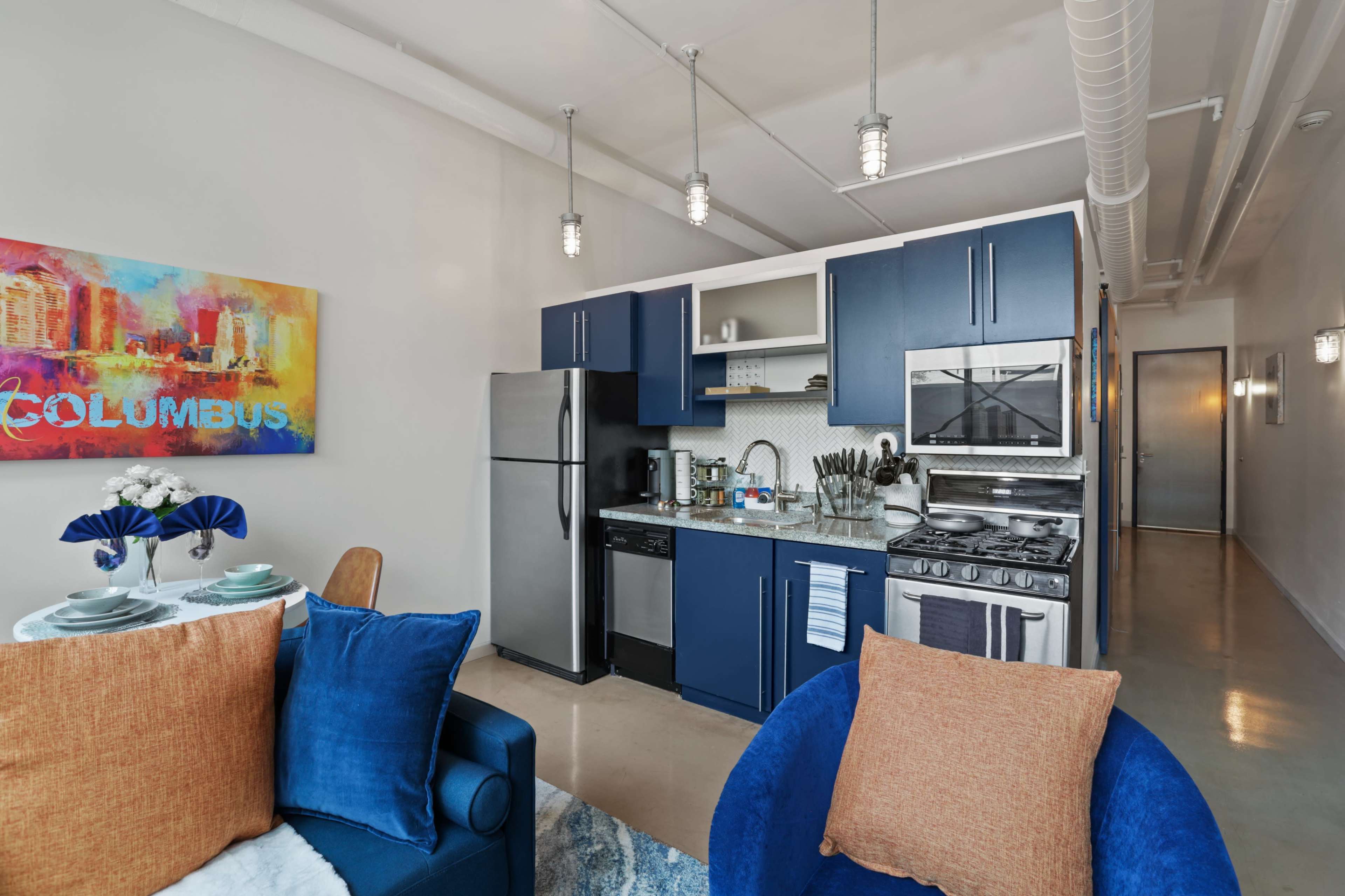 A compact kitchen and dining area featuring blue cabinetry, stainless steel appliances, and a small table set for two.