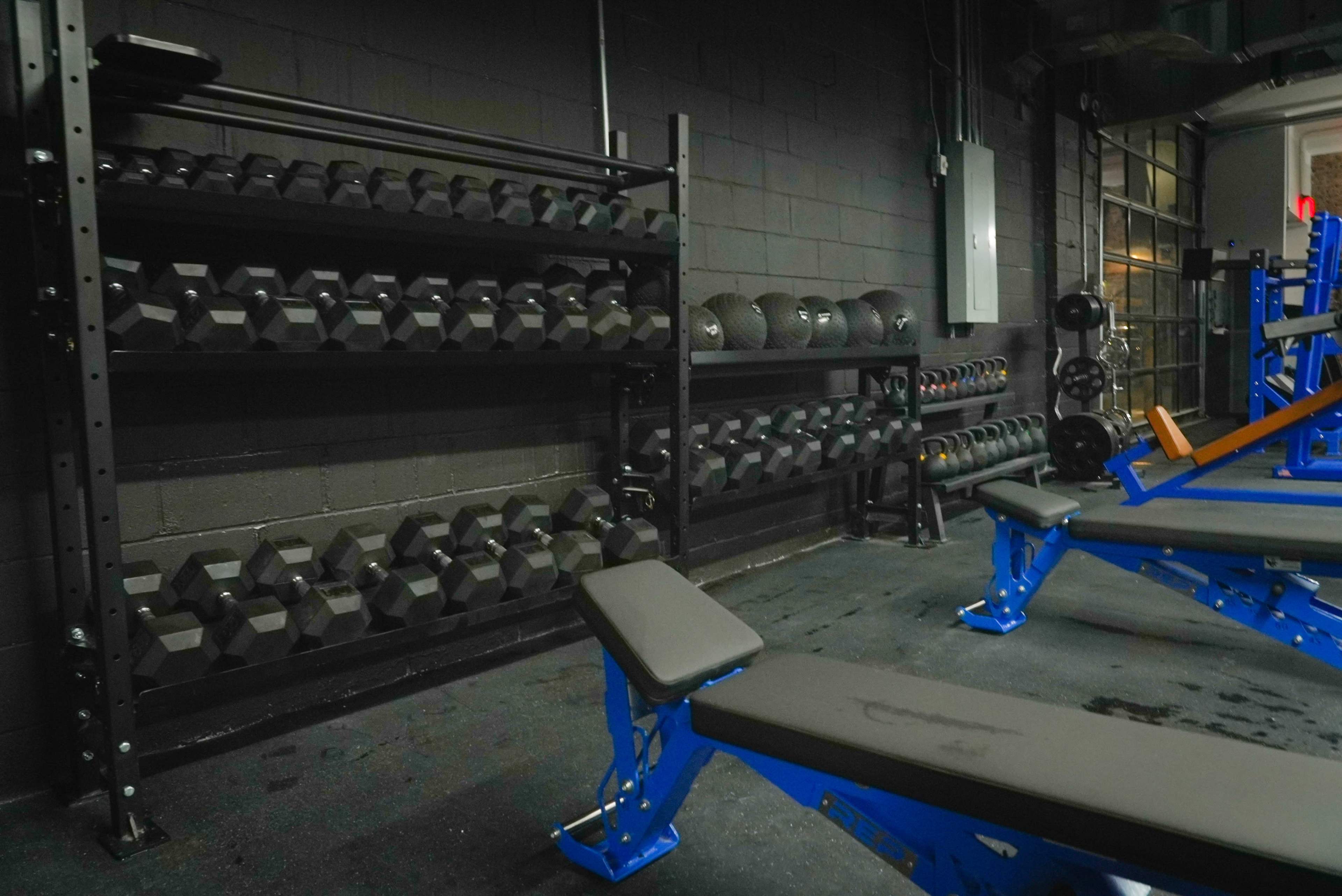 A fitness area with racks of dumbbells and several weight benches against a dark wall.