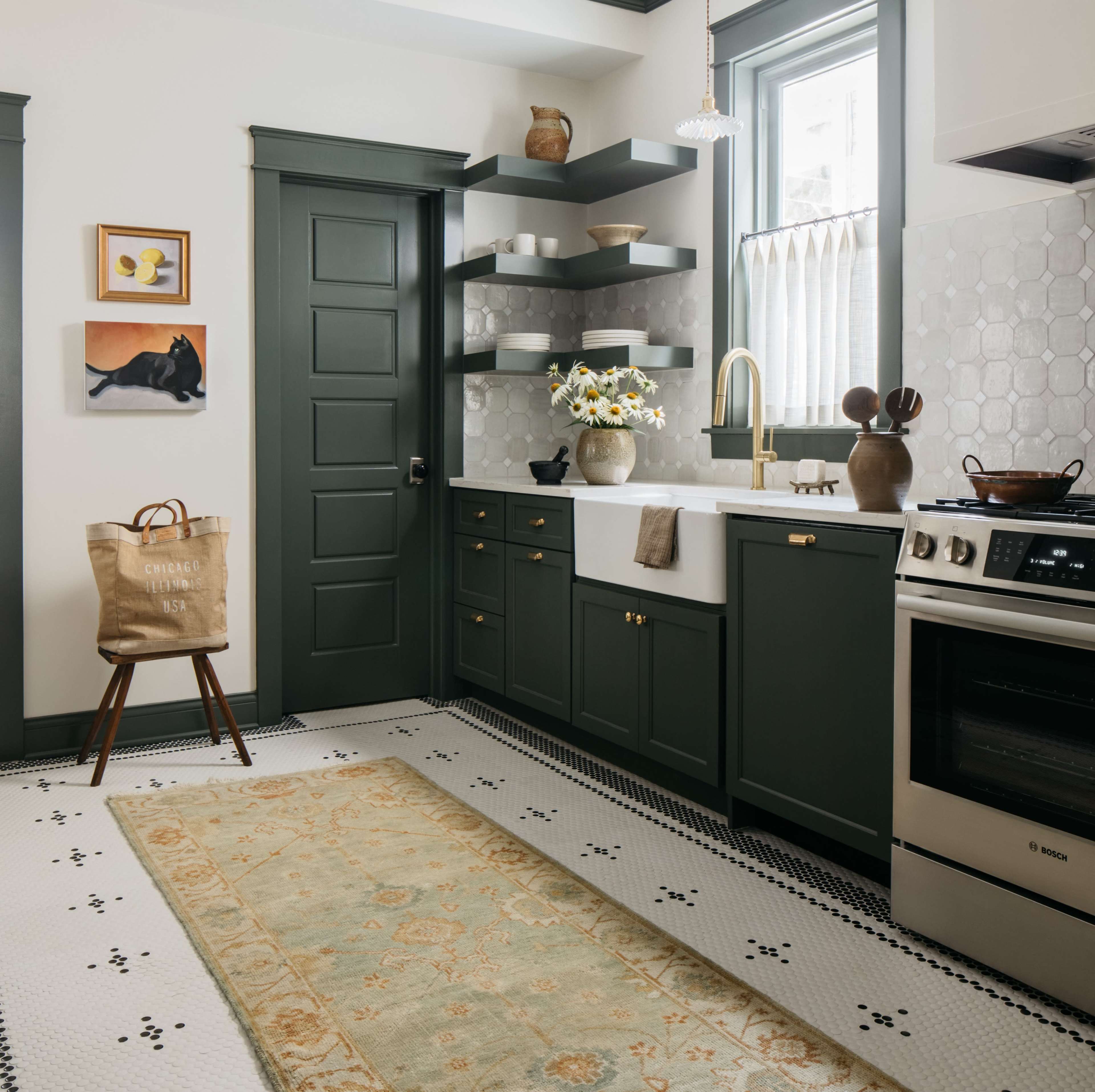 A modern kitchen featuring dark green cabinetry, white countertops, and a decorative rug on a patterned floor.