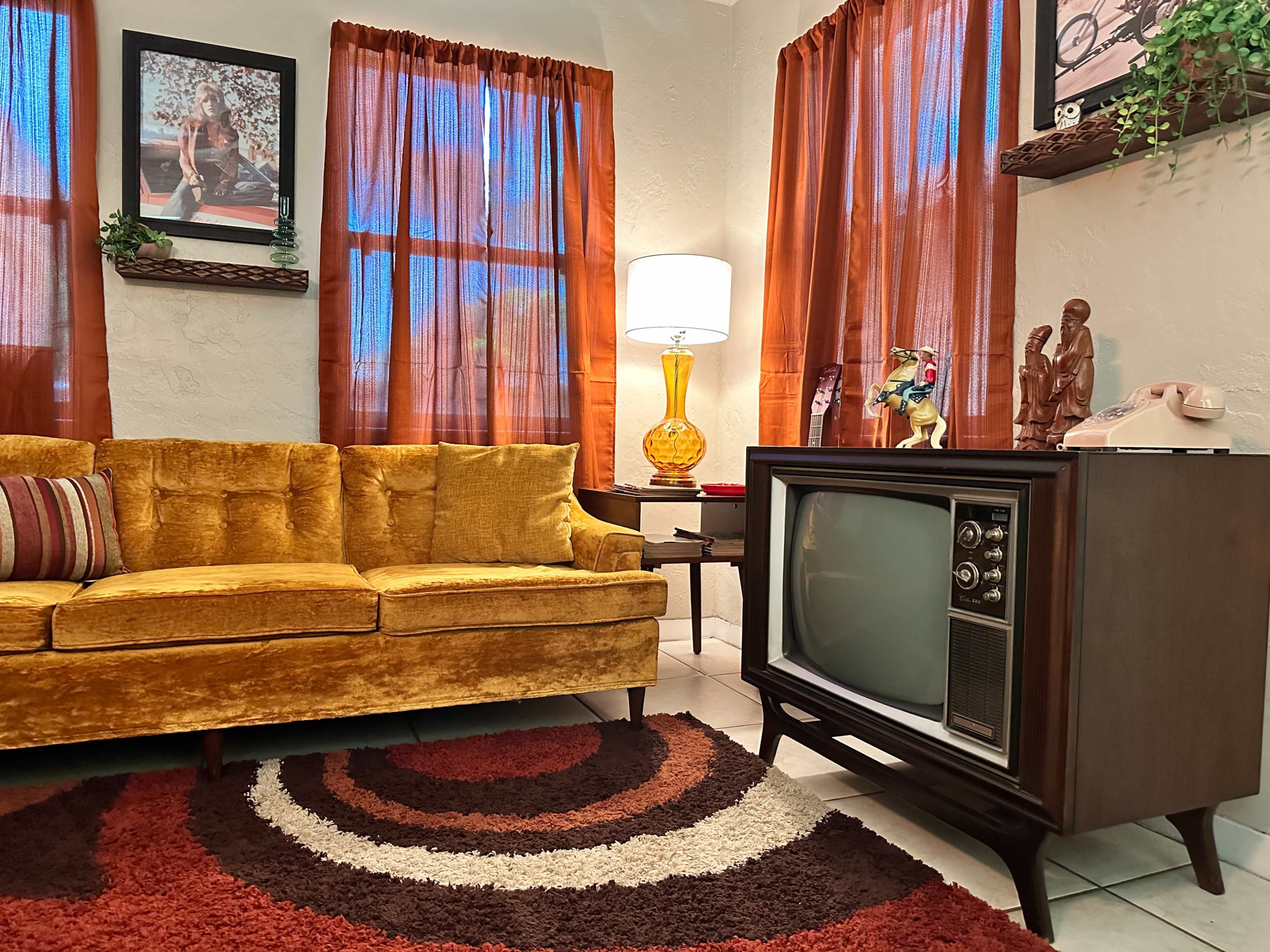 The scene features a vintage living room with a yellow couch, a retro television set, and warm-colored curtains.