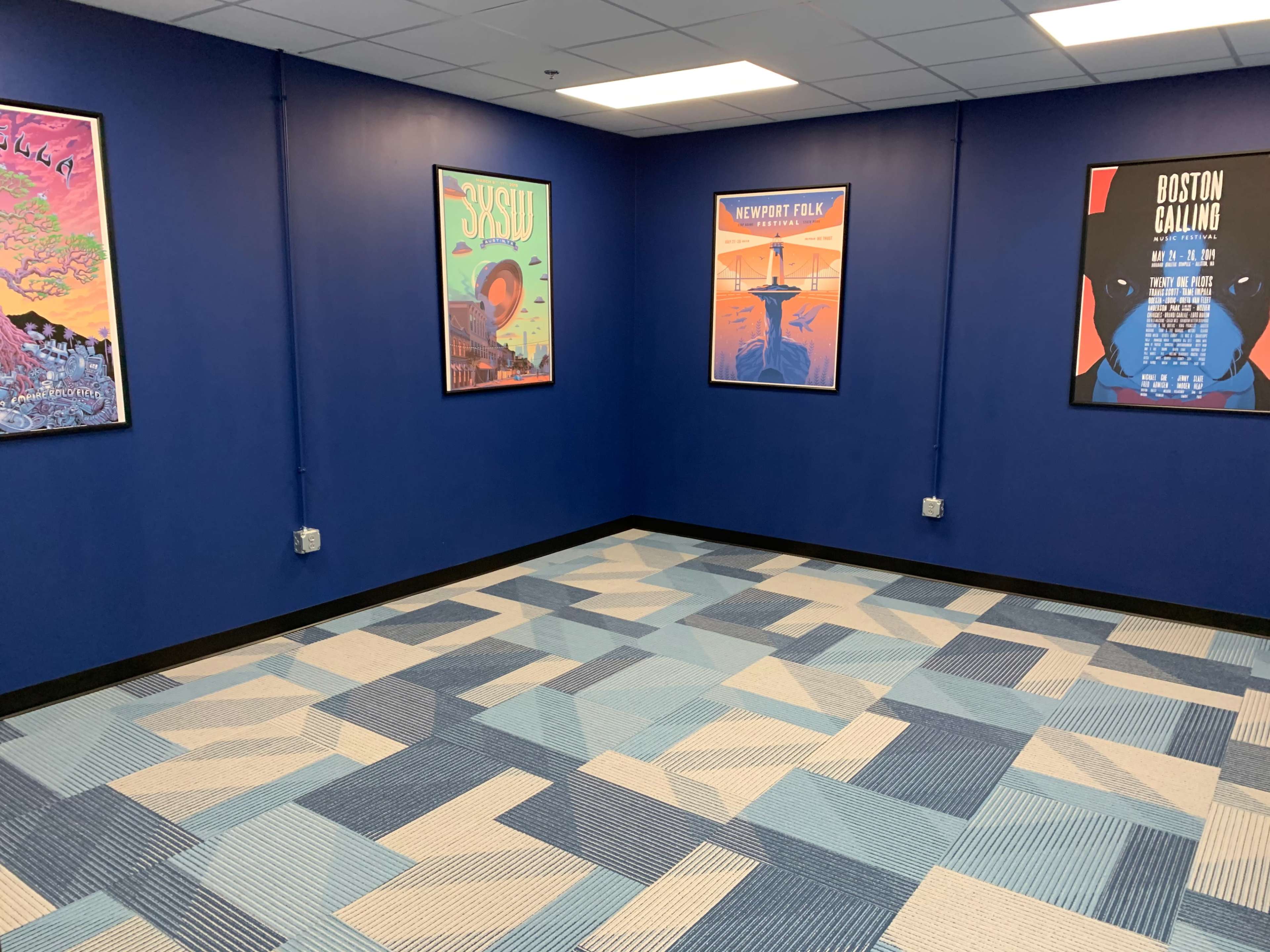 A room with blue walls, a patterned carpet in shades of blue, and framed posters on the walls.