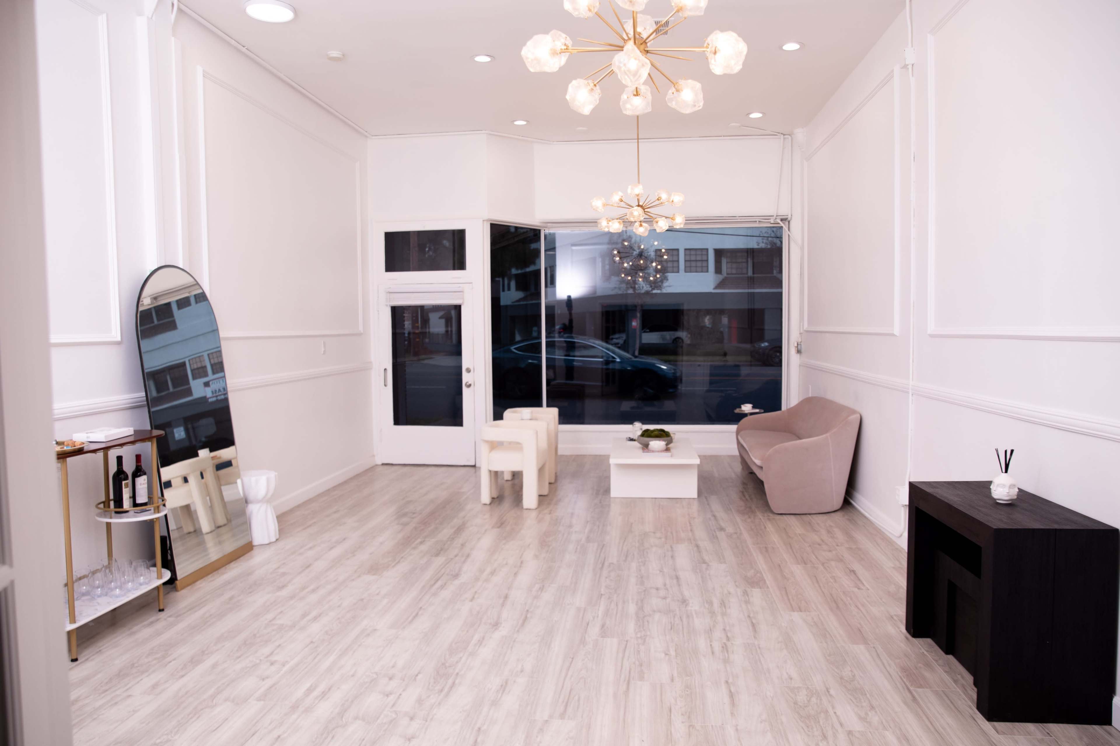 A spacious, minimalist interior with light-colored flooring, a large window facing the street, and a few pieces of furniture including a sofa and a small table.