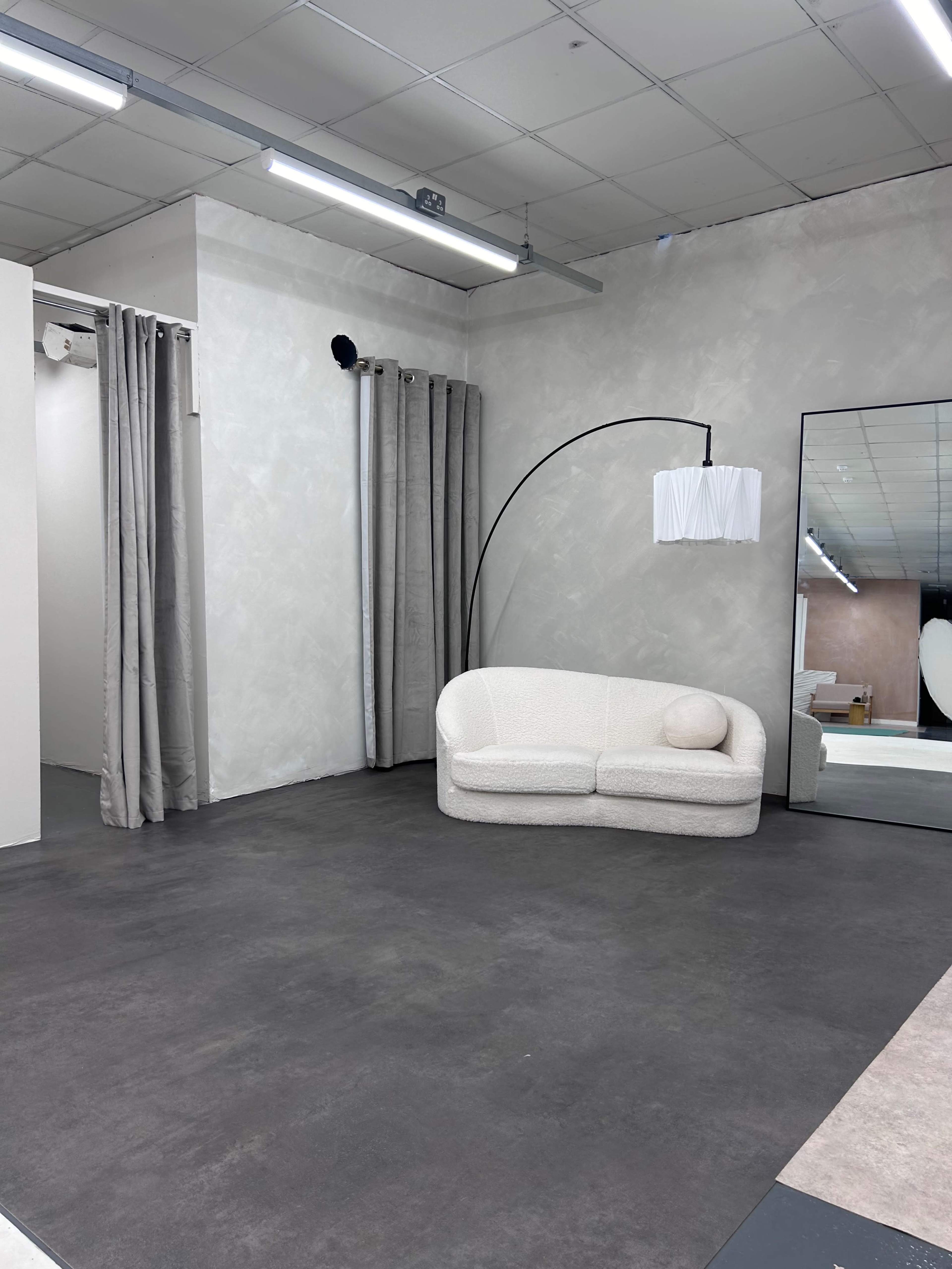 A minimalist interior space featuring a curved sofa, a floor lamp, and a large mirrored wall.