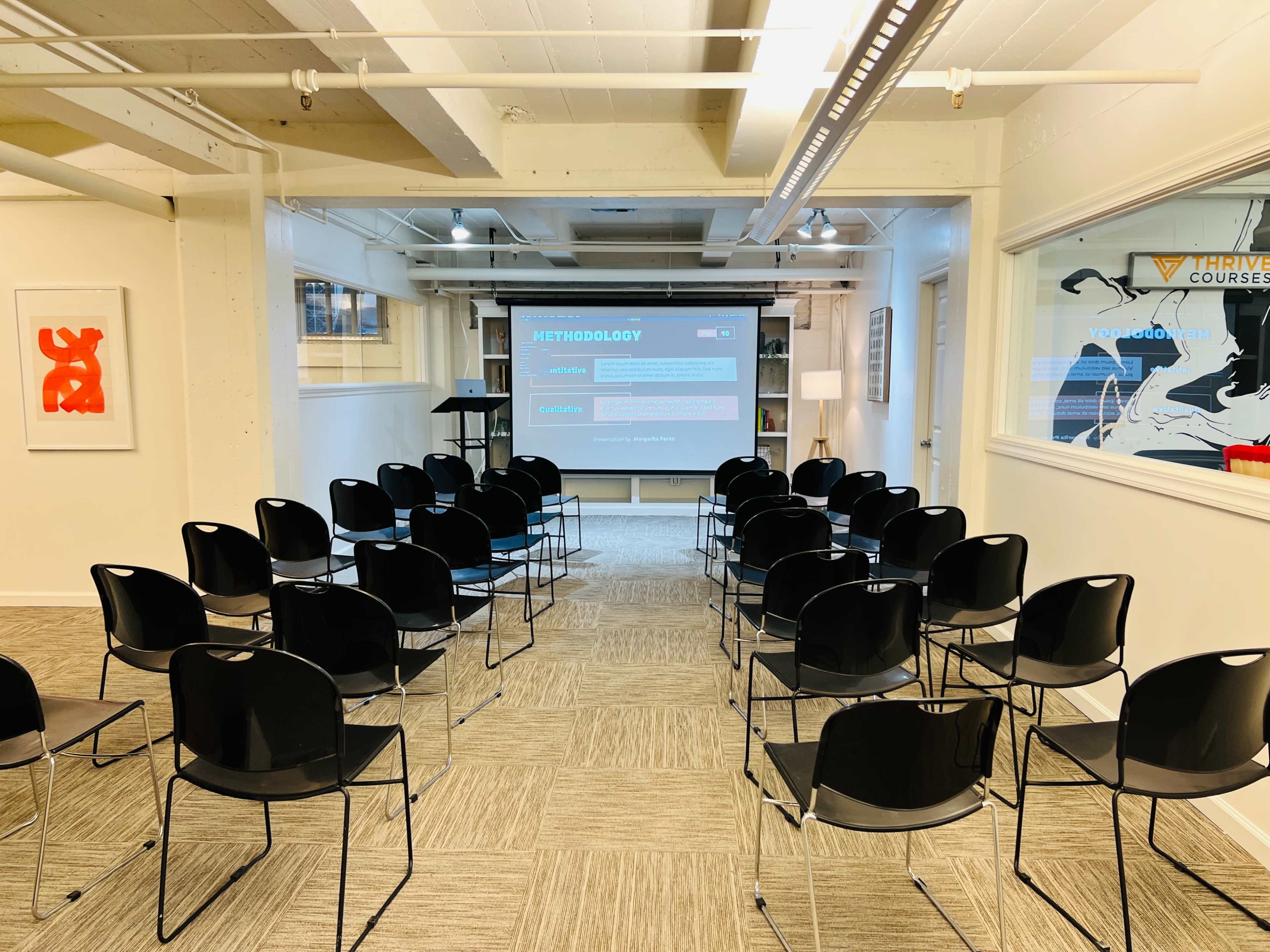 A row of black chairs is set up in a well-lit room facing a projection screen that displays the word "METHODOLOGY."