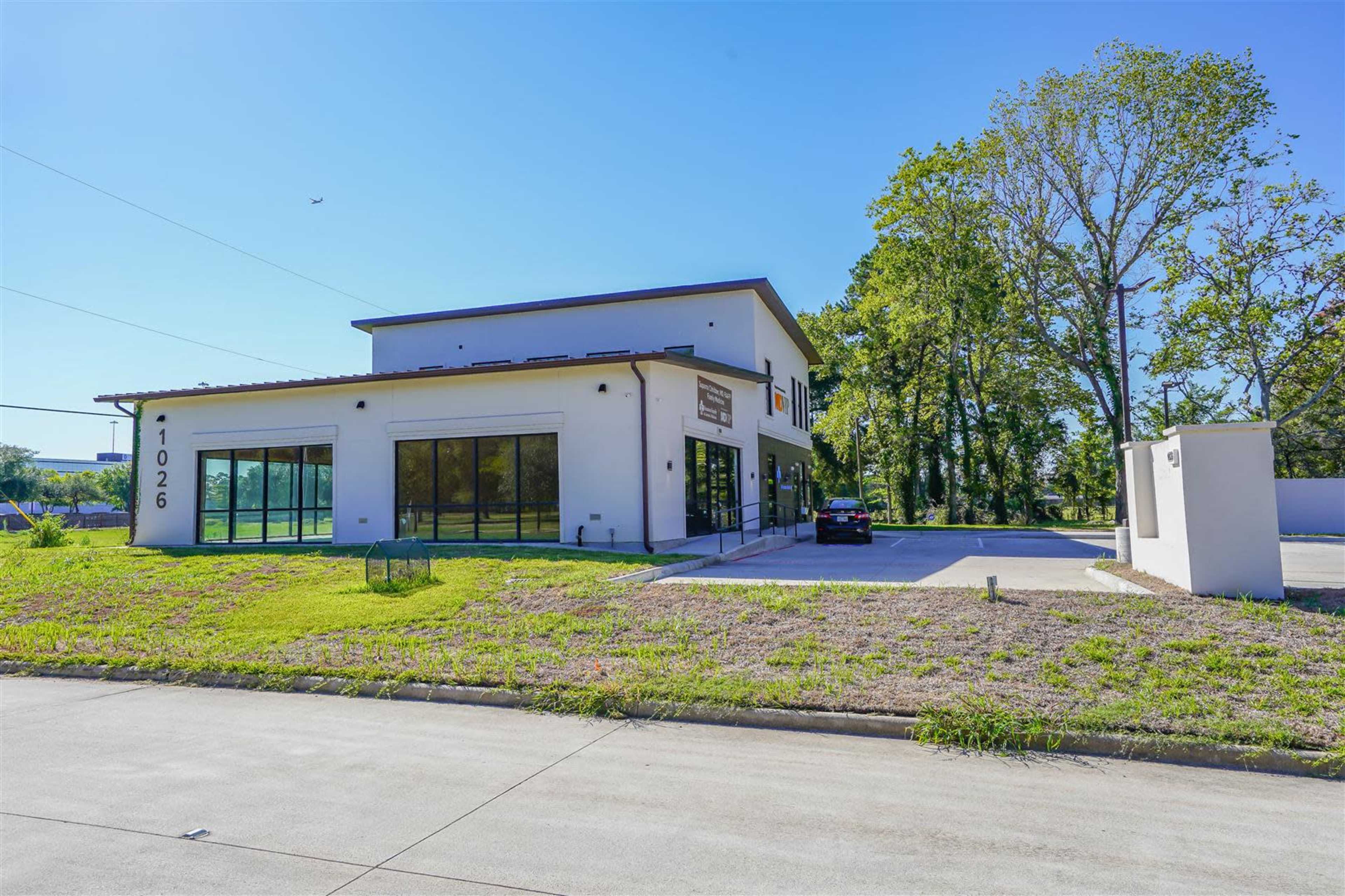 A modern building with large windows and a parking area is situated on a grassy lot beside a paved road.