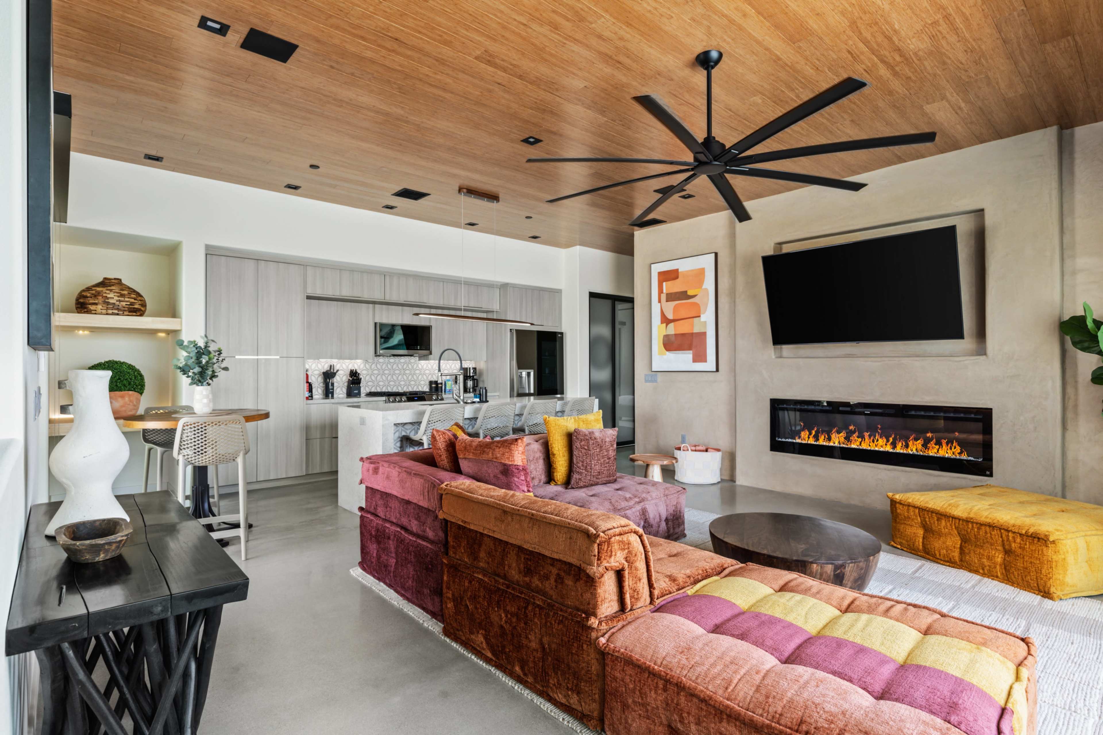 The image shows a modern living room featuring a sectional sofa, a sleek fireplace, and a kitchen area in the background.