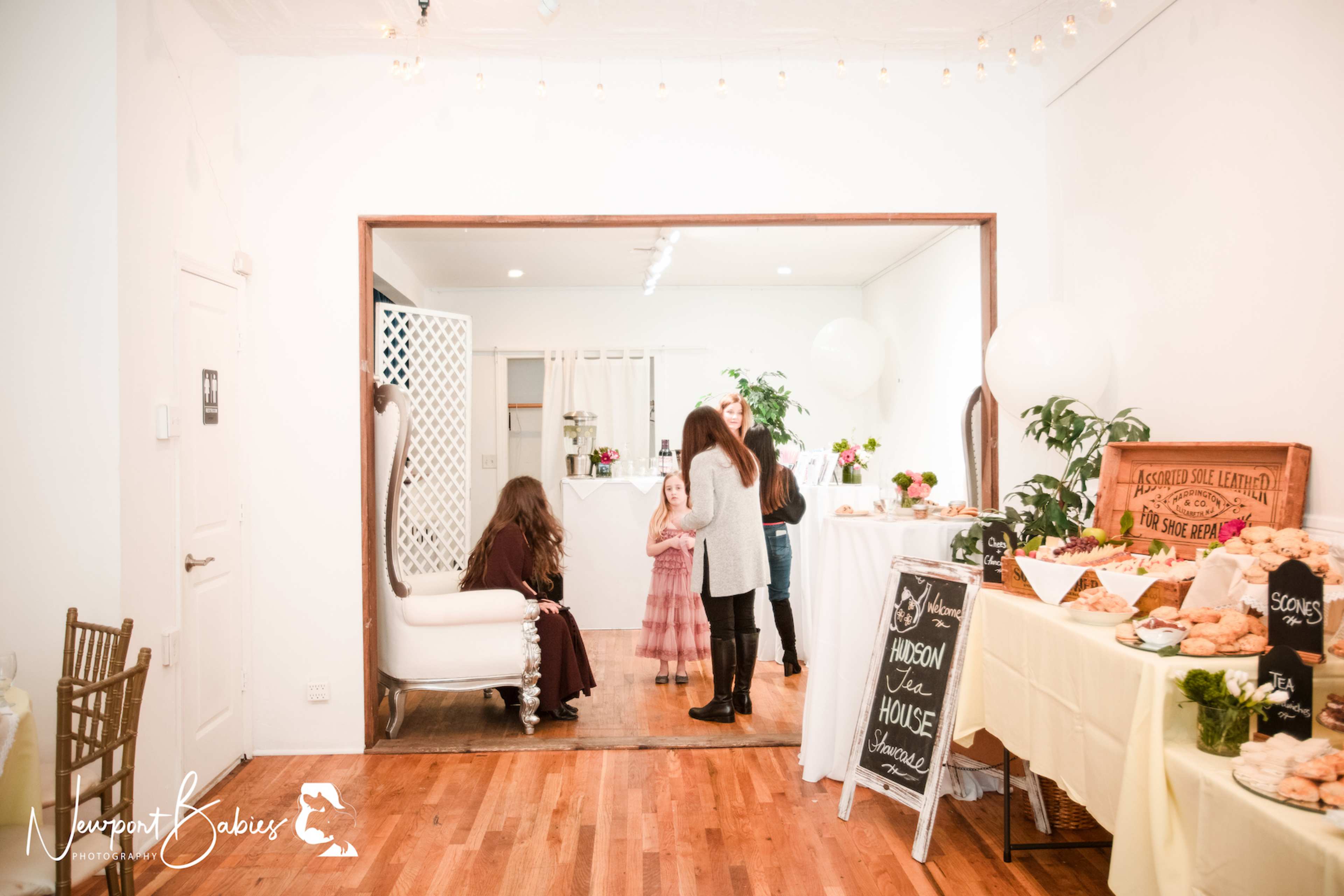 A bright room with a seating area, guests engaging in conversation, and a table set with various food items including pastries and drinks.