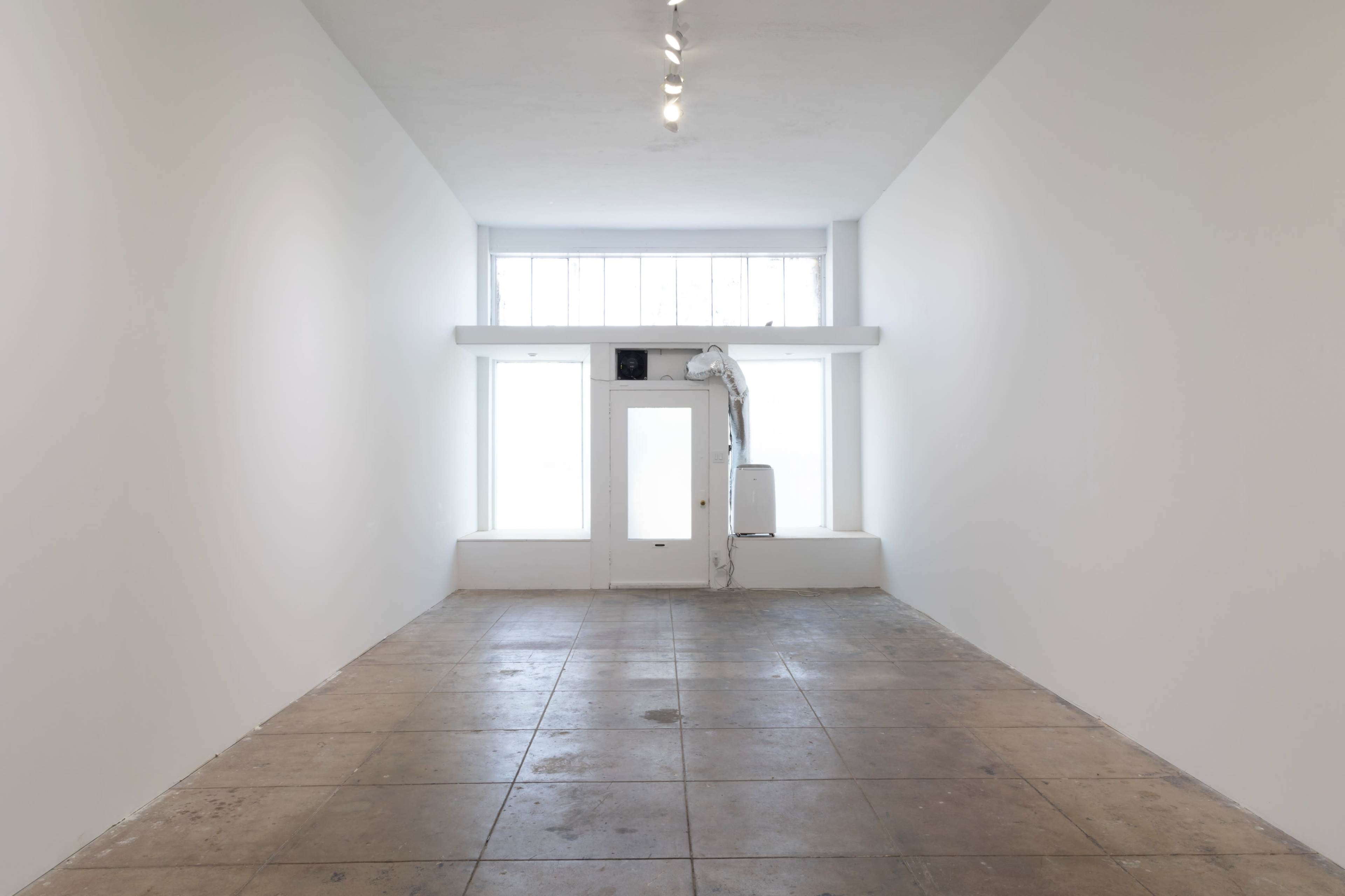 A minimalist, empty gallery space with large windows and a single door at the far end.