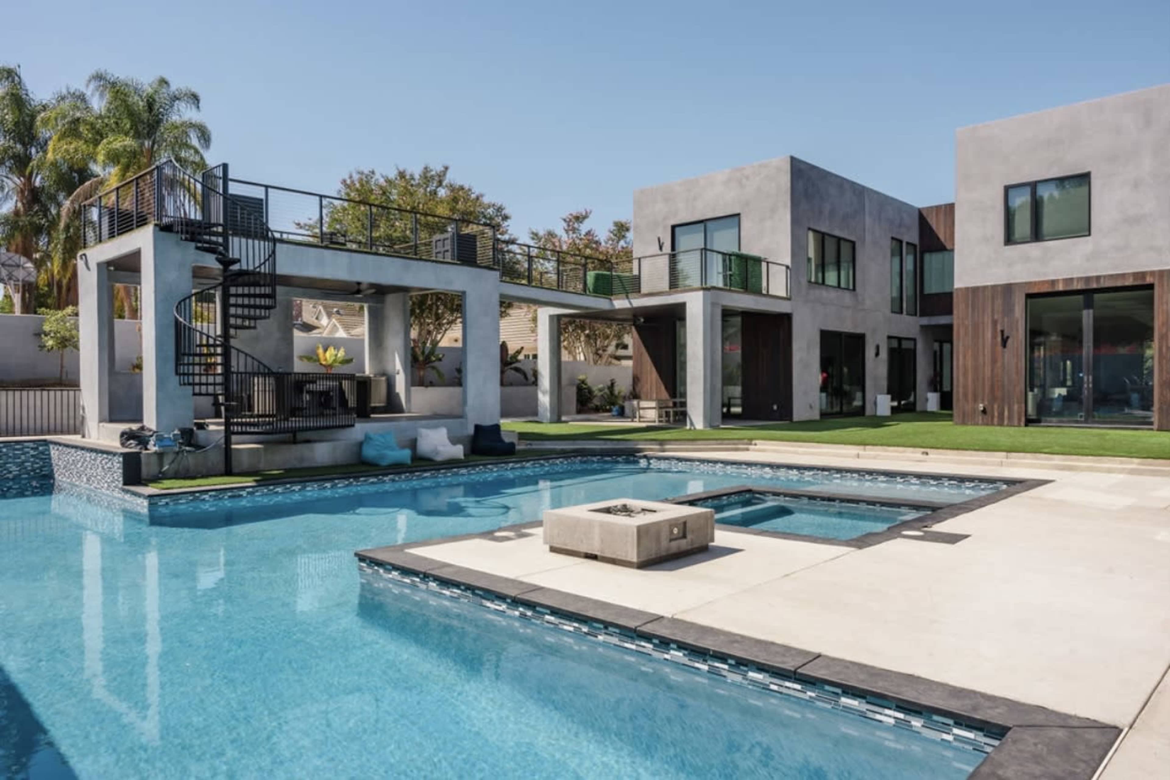 A modern home with two distinct buildings surrounding a swimming pool, featuring a spiral staircase and a landscaped yard.
