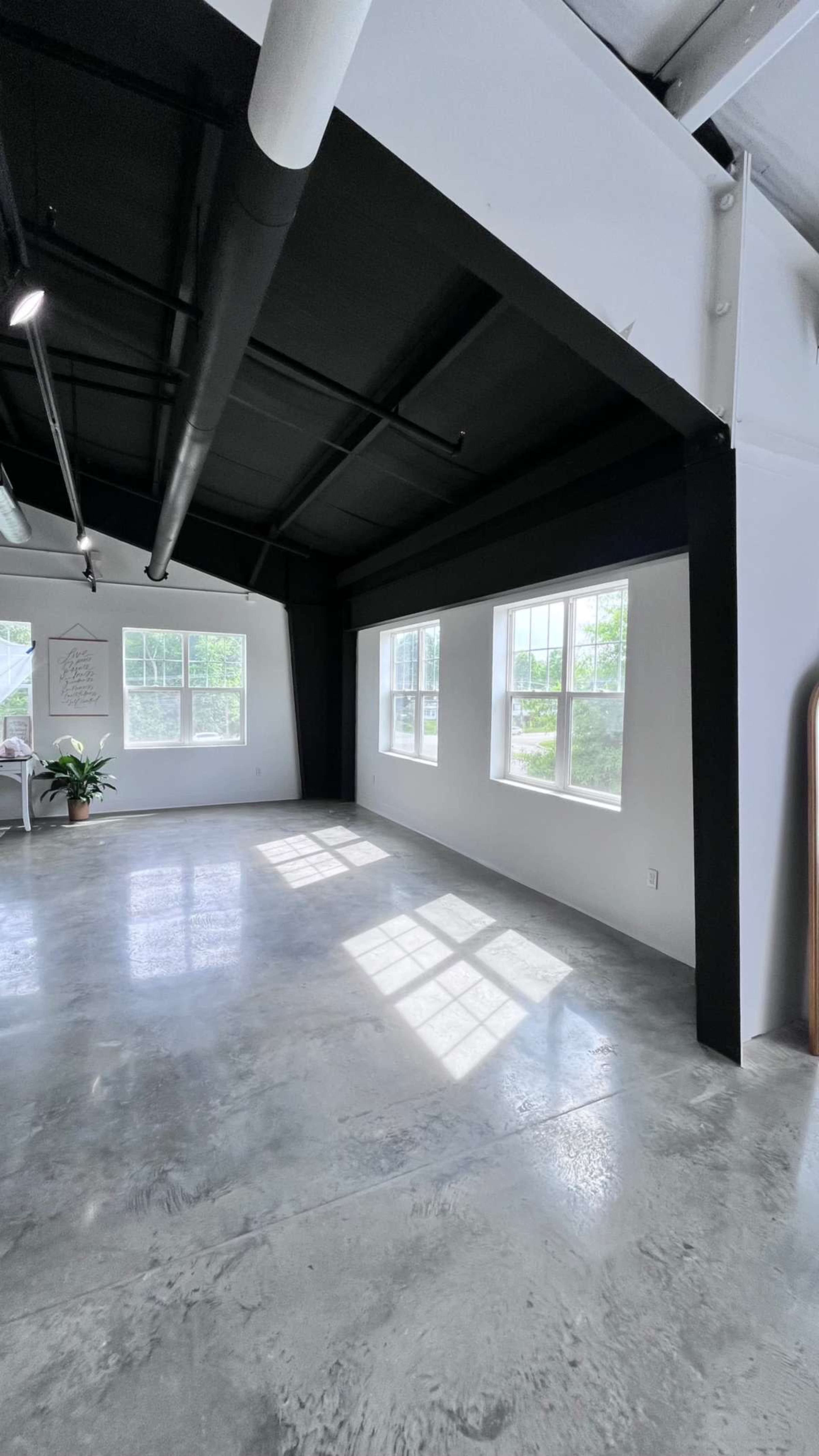 The image shows an empty room with polished concrete floors, large windows, and a black ceiling.