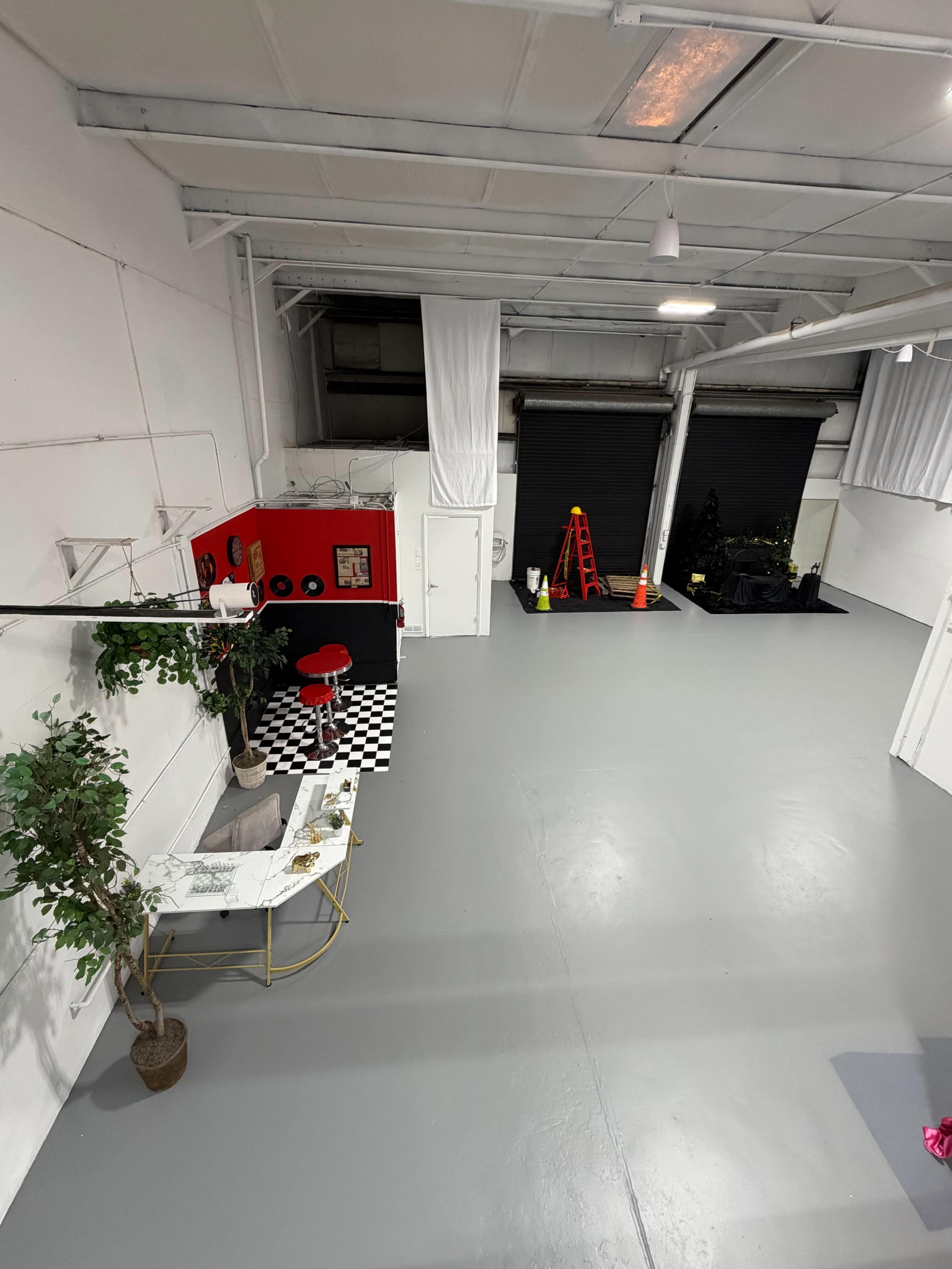 The image shows a large, mostly empty gray room with a red vending machine, a checkered floor area, and a couple of ladders against a dark wall.