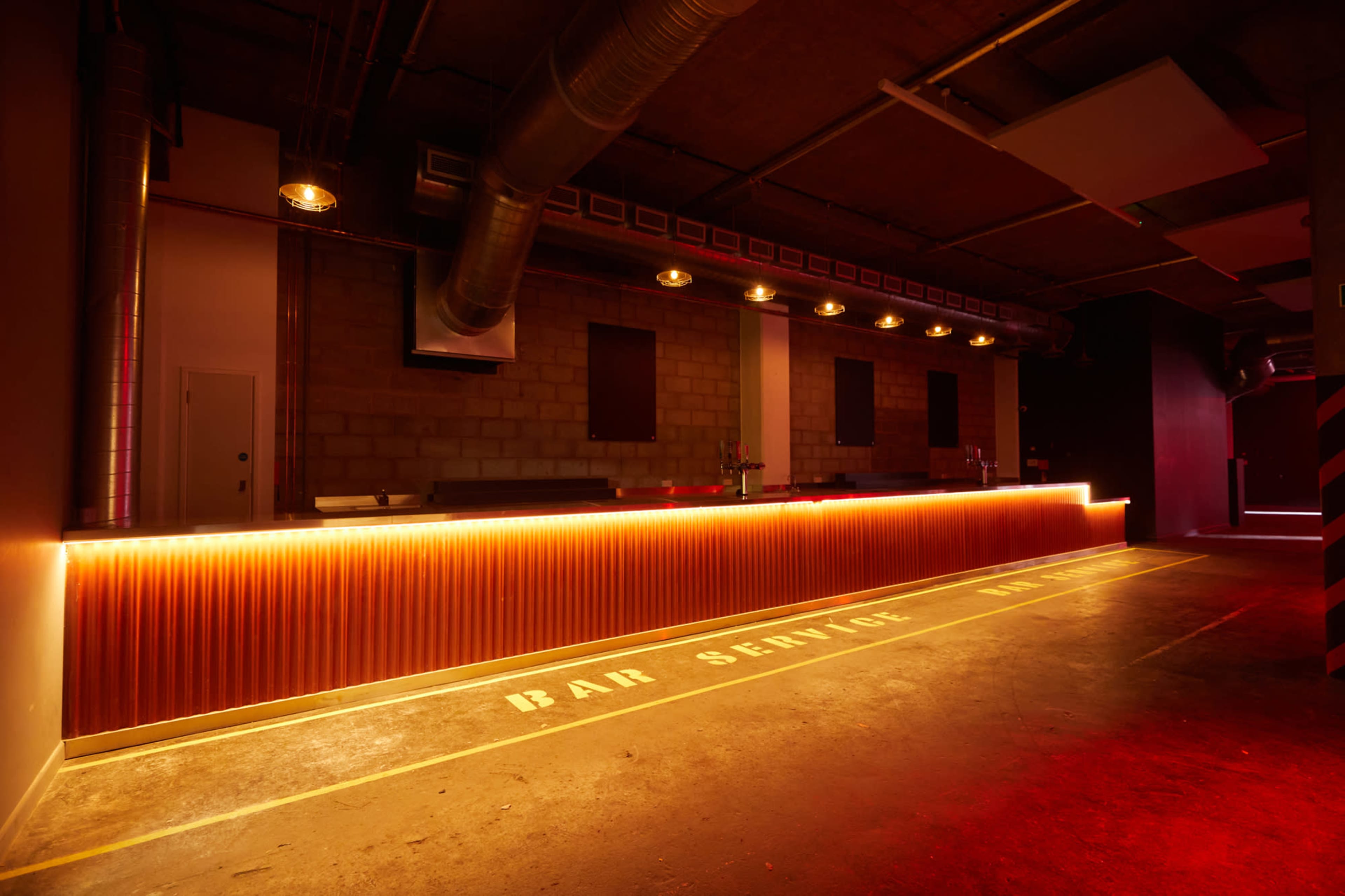 A dimly lit bar area with a long, illuminated counter and a concrete floor marked with the words "BAR SERVICE."
