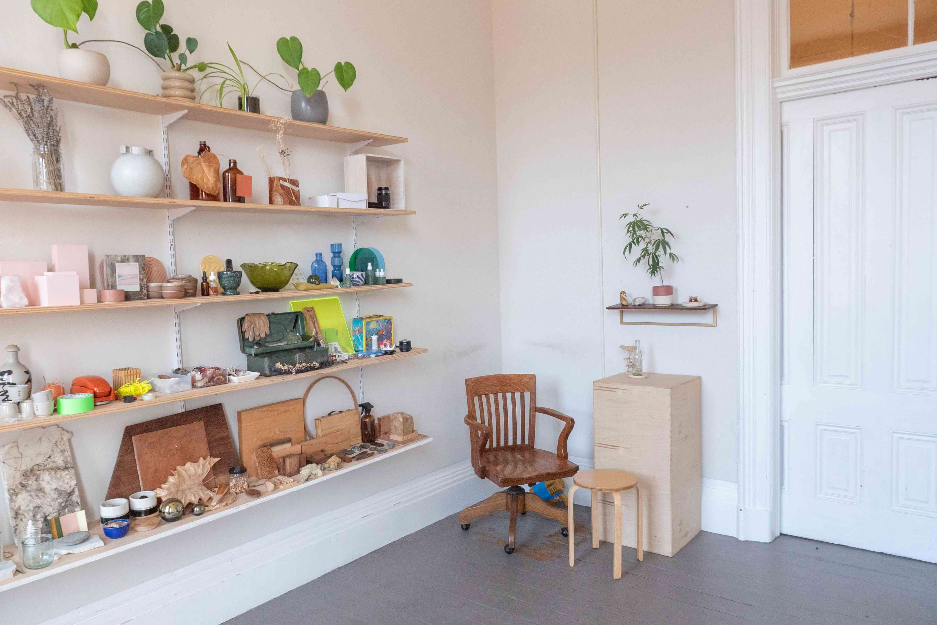 The image shows a room with a wooden shelf displaying various decorative items, a chair, and a small table in a corner.