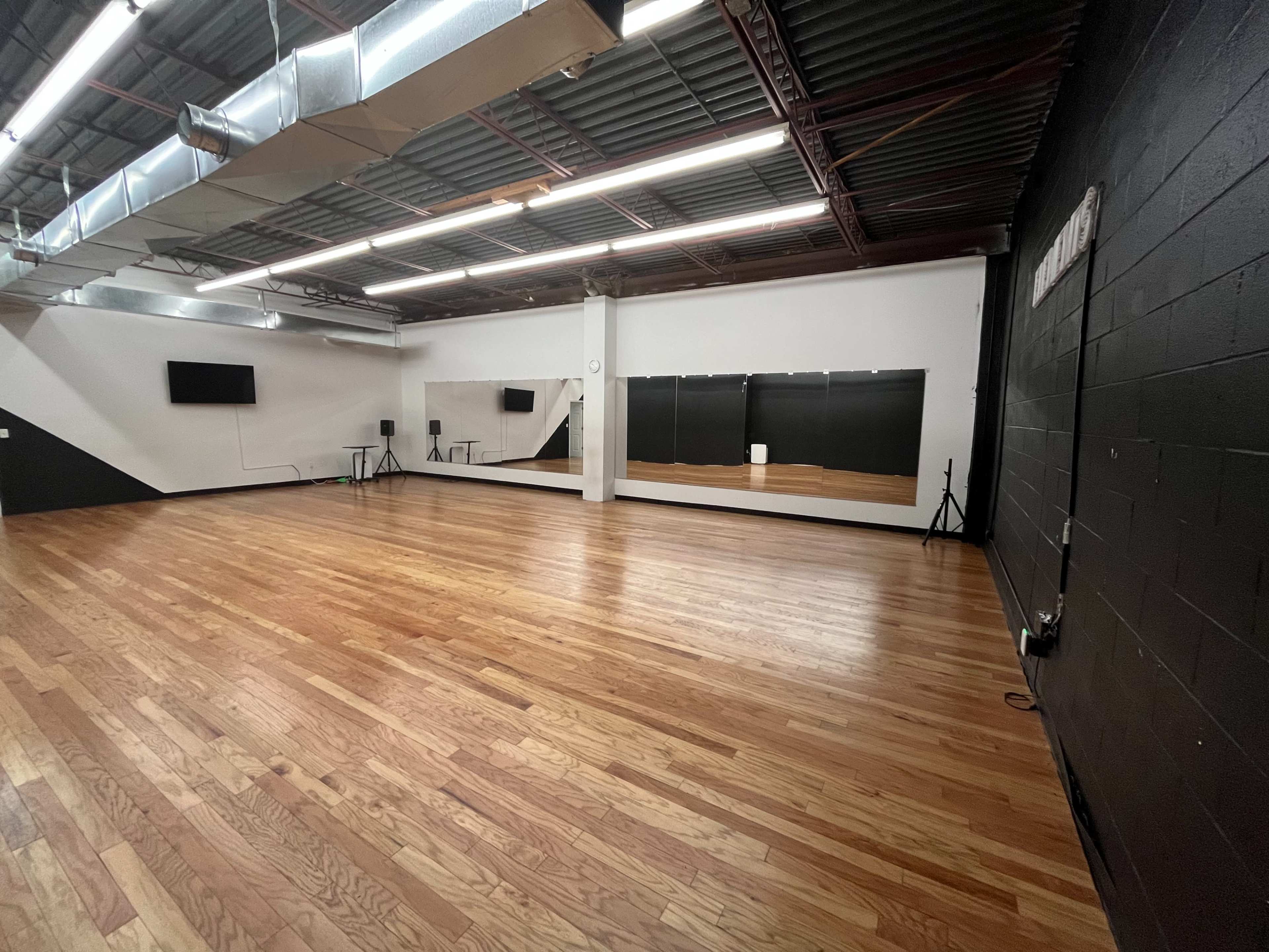An empty dance studio with wooden floors, mirrors on one wall, and minimal equipment in the corners.