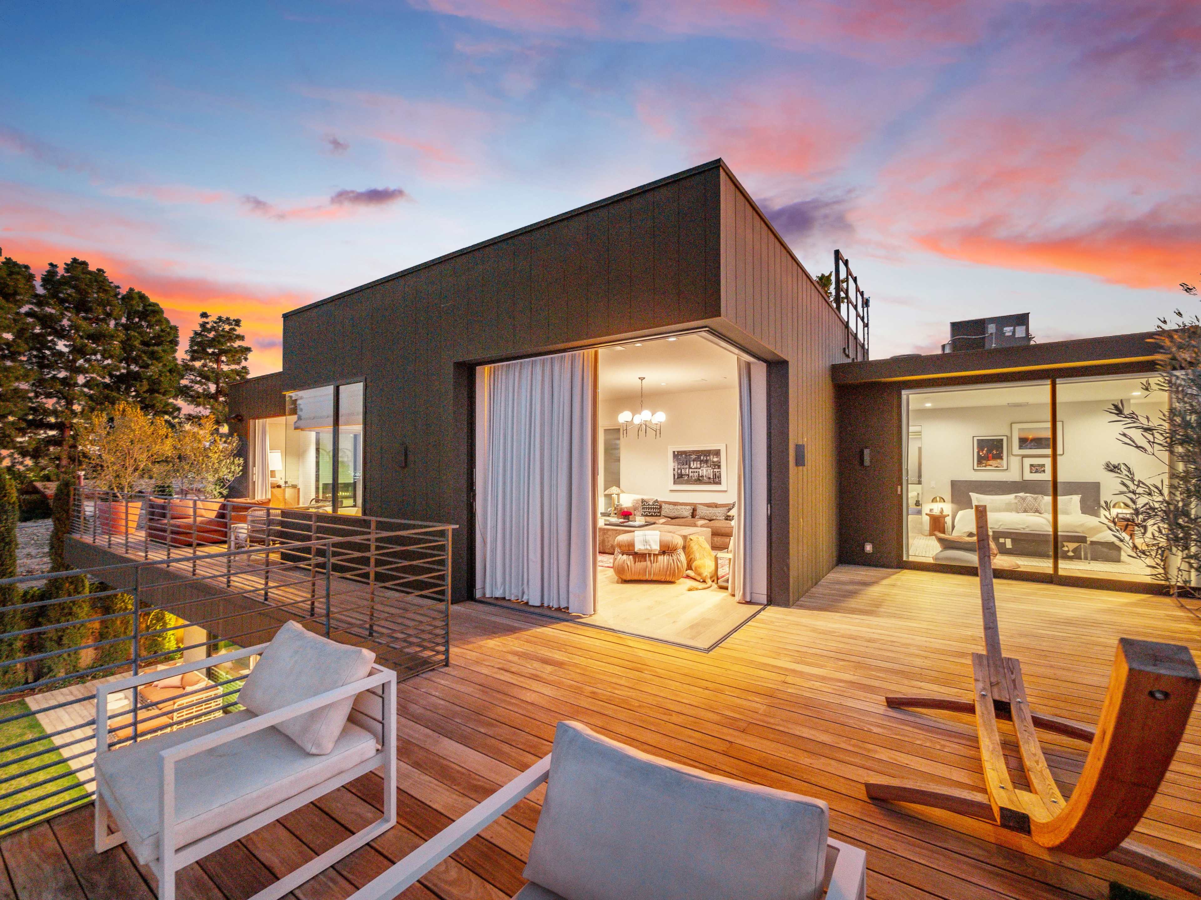 A modern home with a spacious wooden deck overlooking a landscaped area at sunset.