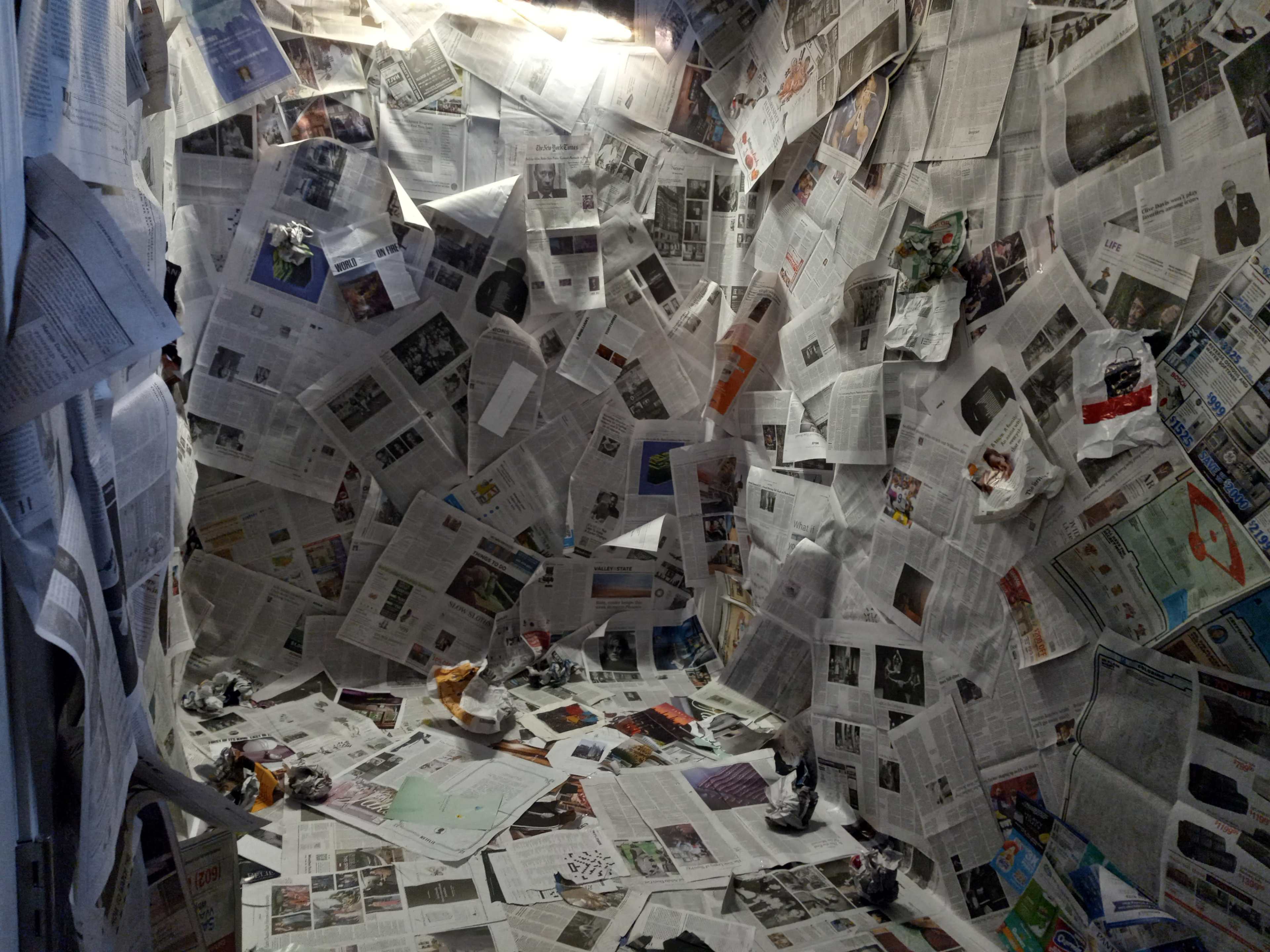 The image shows a small enclosed space covered with crumpled newspapers on the walls and floor.