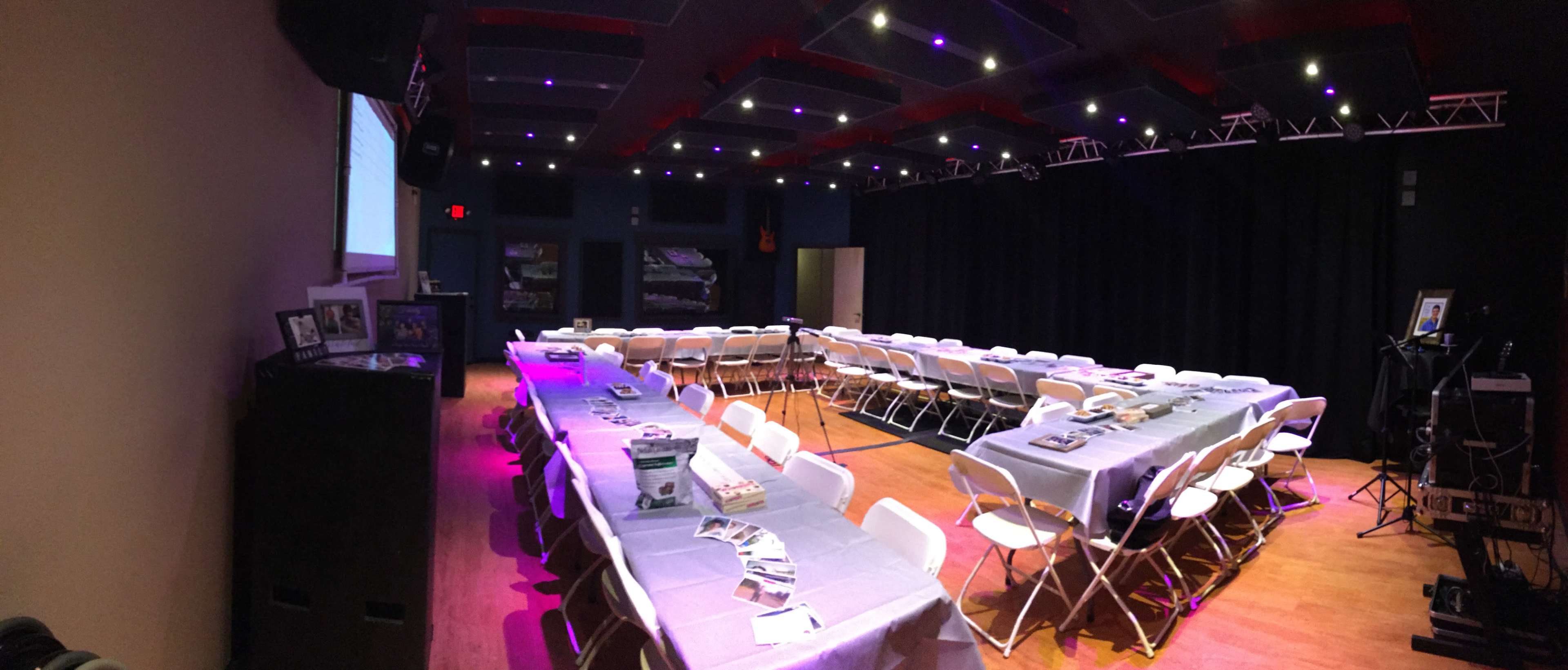 A spacious room is set up with white folding chairs arranged around a central area, decorated with gray tablecloths and promotional materials on each table.
