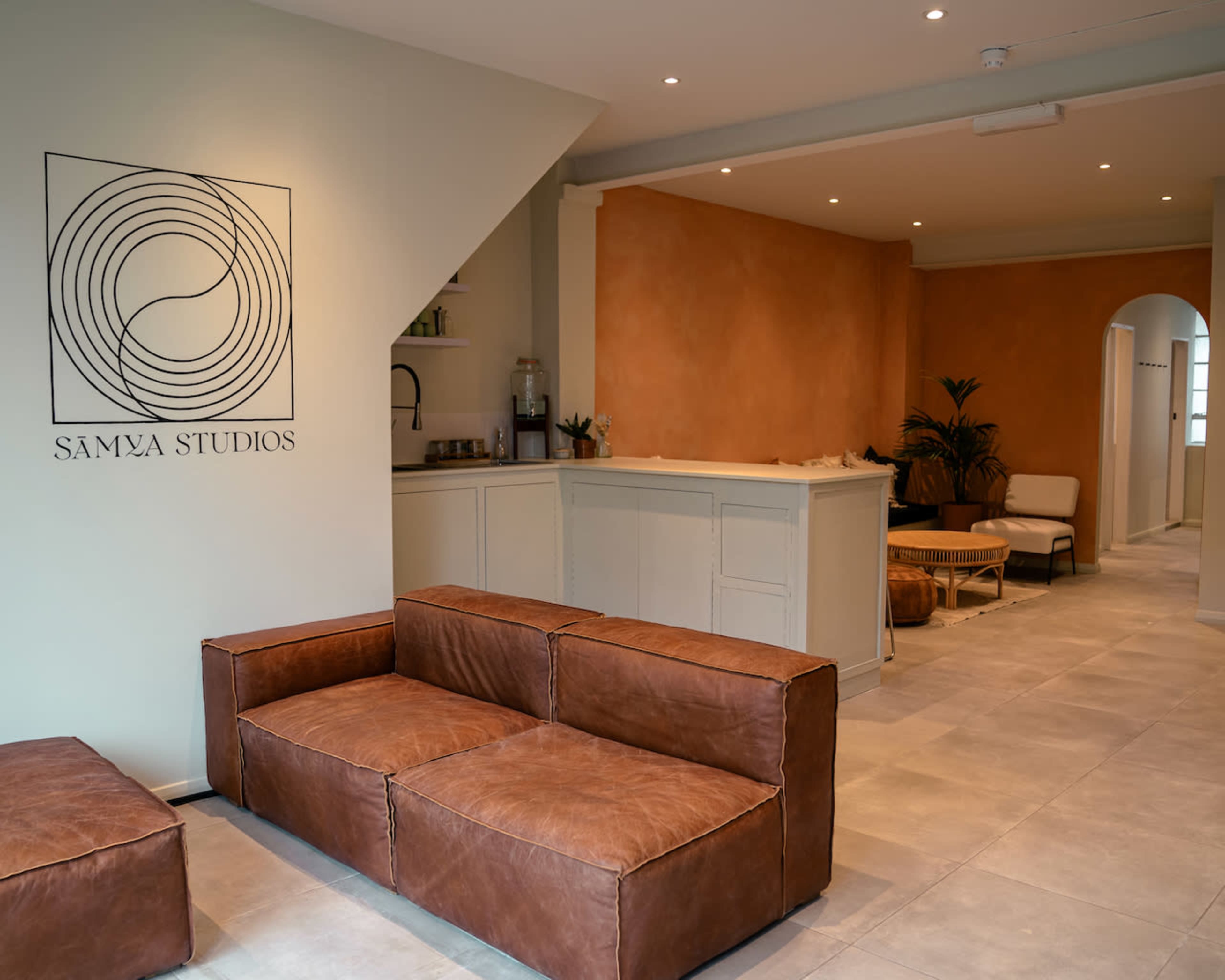 A modern studio reception area with a brown leather couch, a light-colored counter, and warm-toned walls.