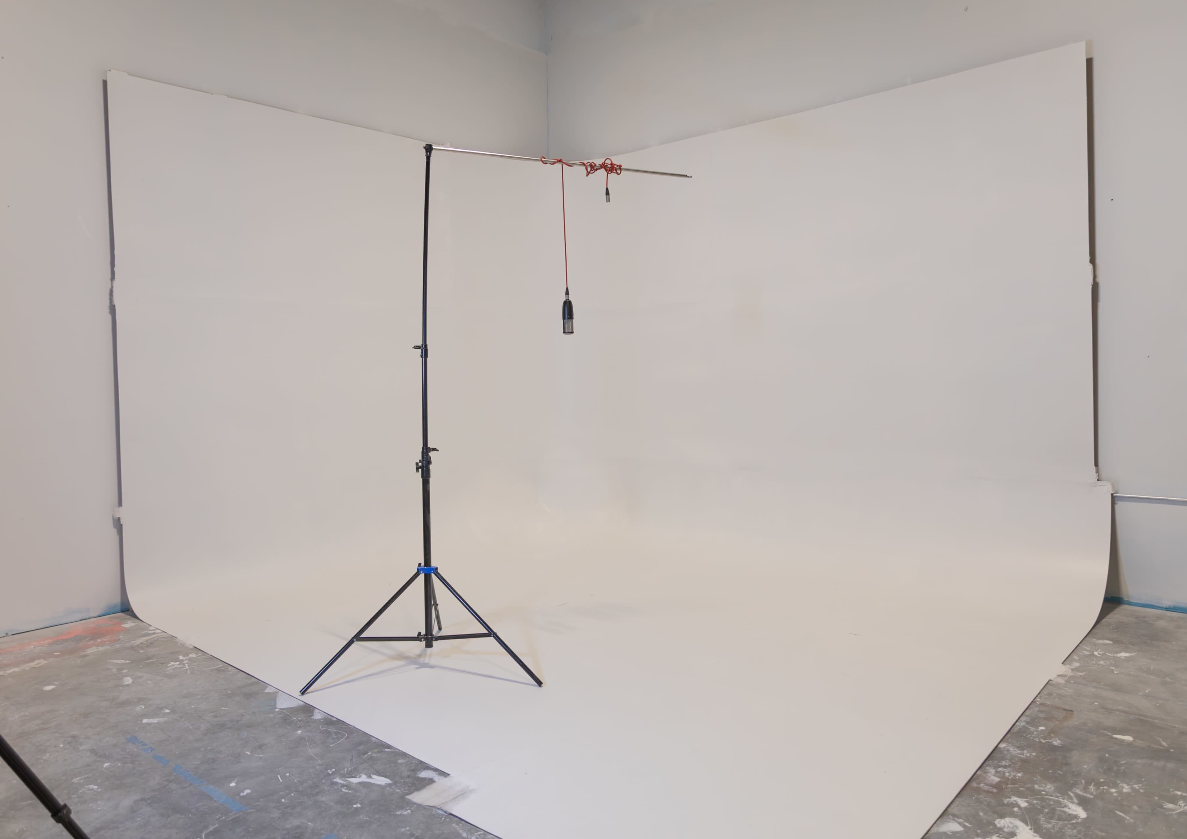 The image shows a photography studio with a seamless white backdrop and a lighting stand set up in the corner.