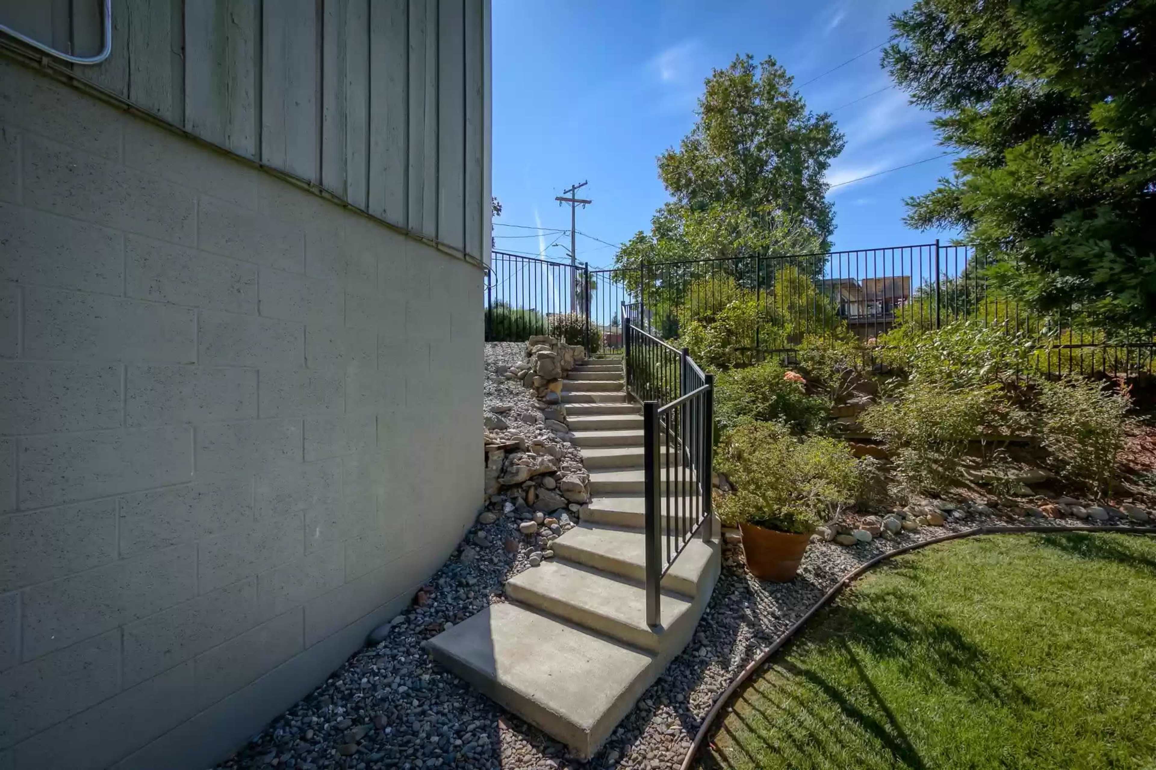 Stairs leading up from a gravel path to a landscaped area surrounded by a metal railing and greenery.