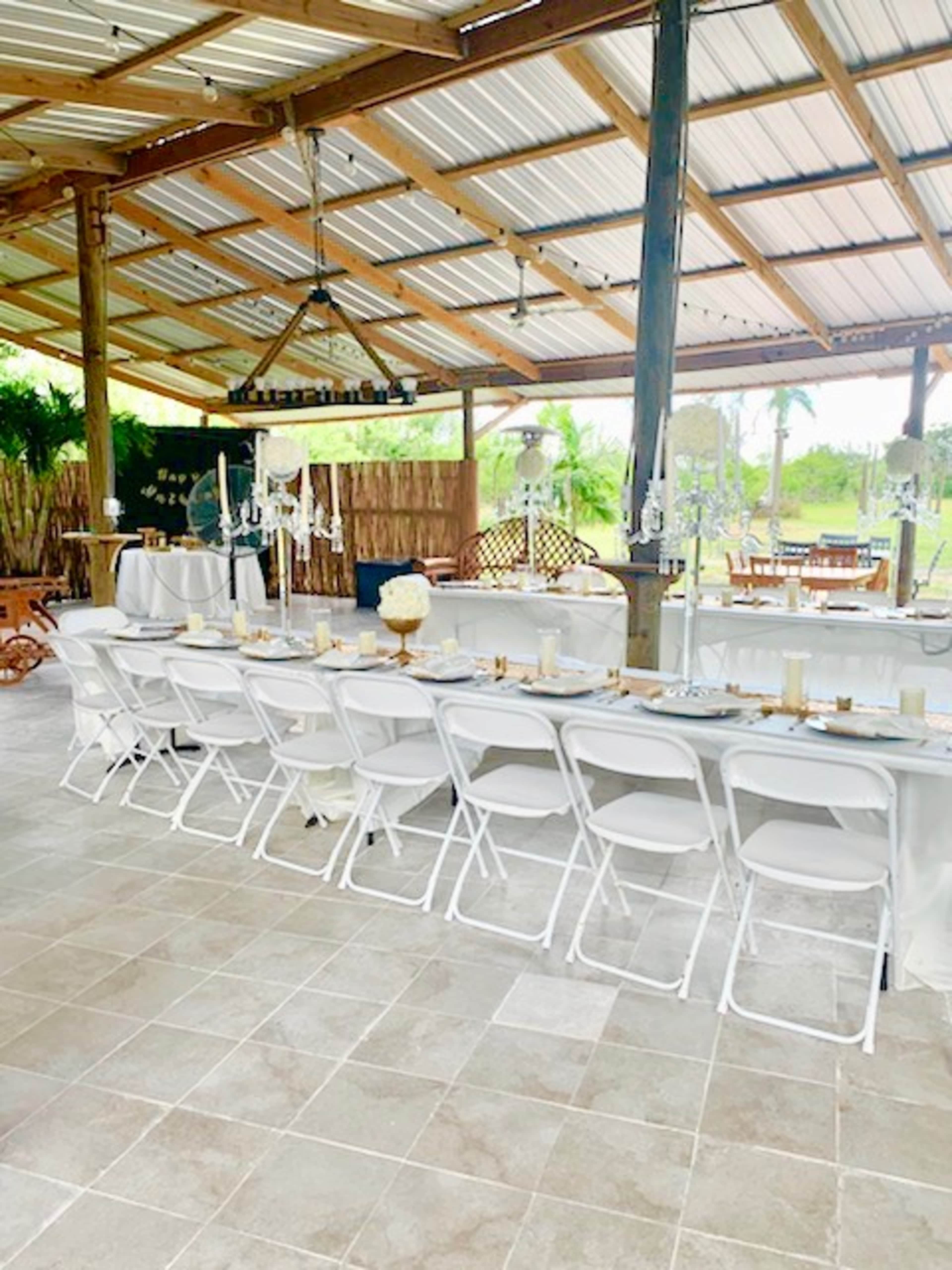 The image shows a decorated reception area with rows of white folding chairs set around a long table under a covered structure.