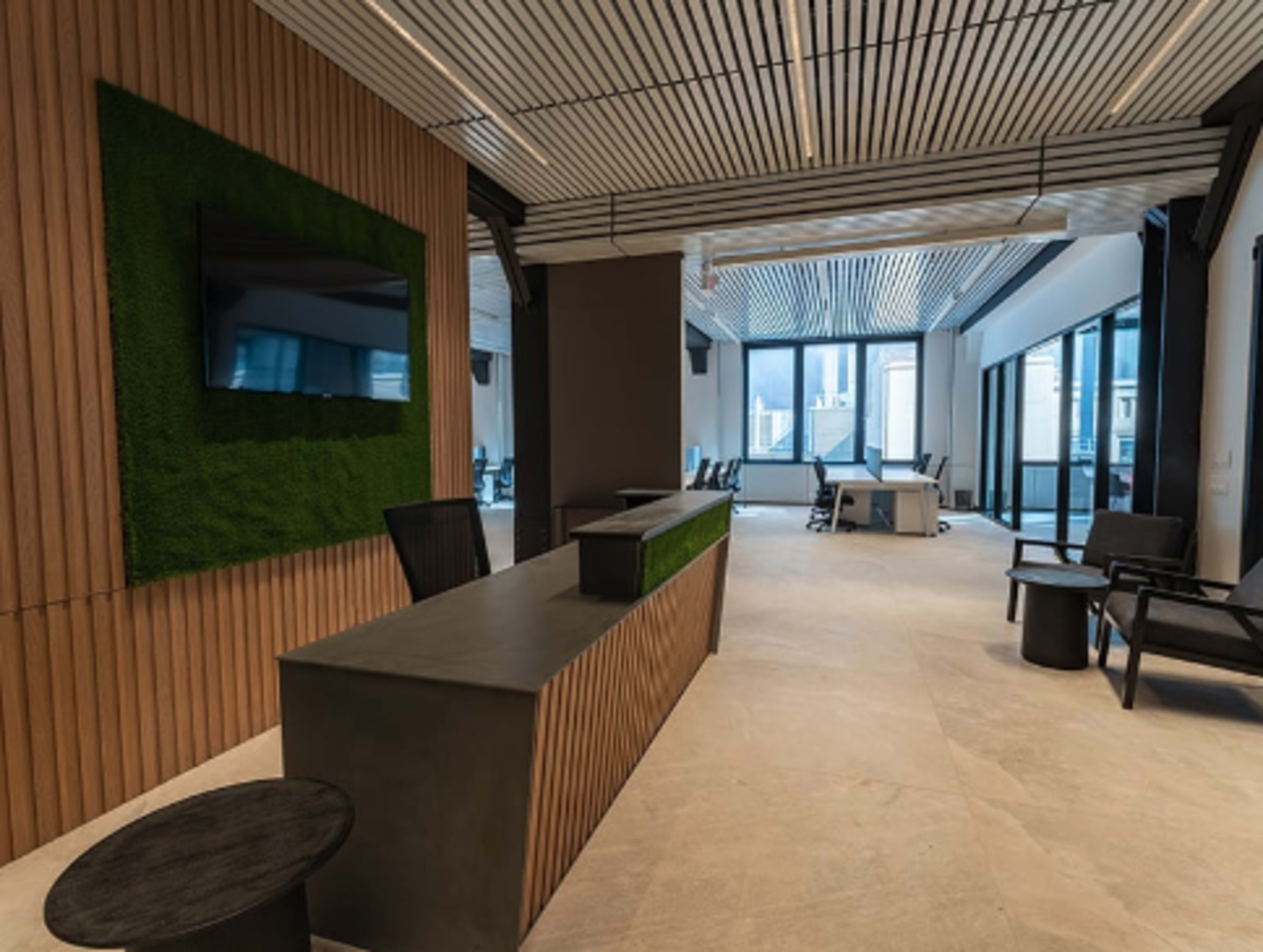 The image shows a modern office interior featuring a reception area with a green wall, large windows, and minimalistic furniture.