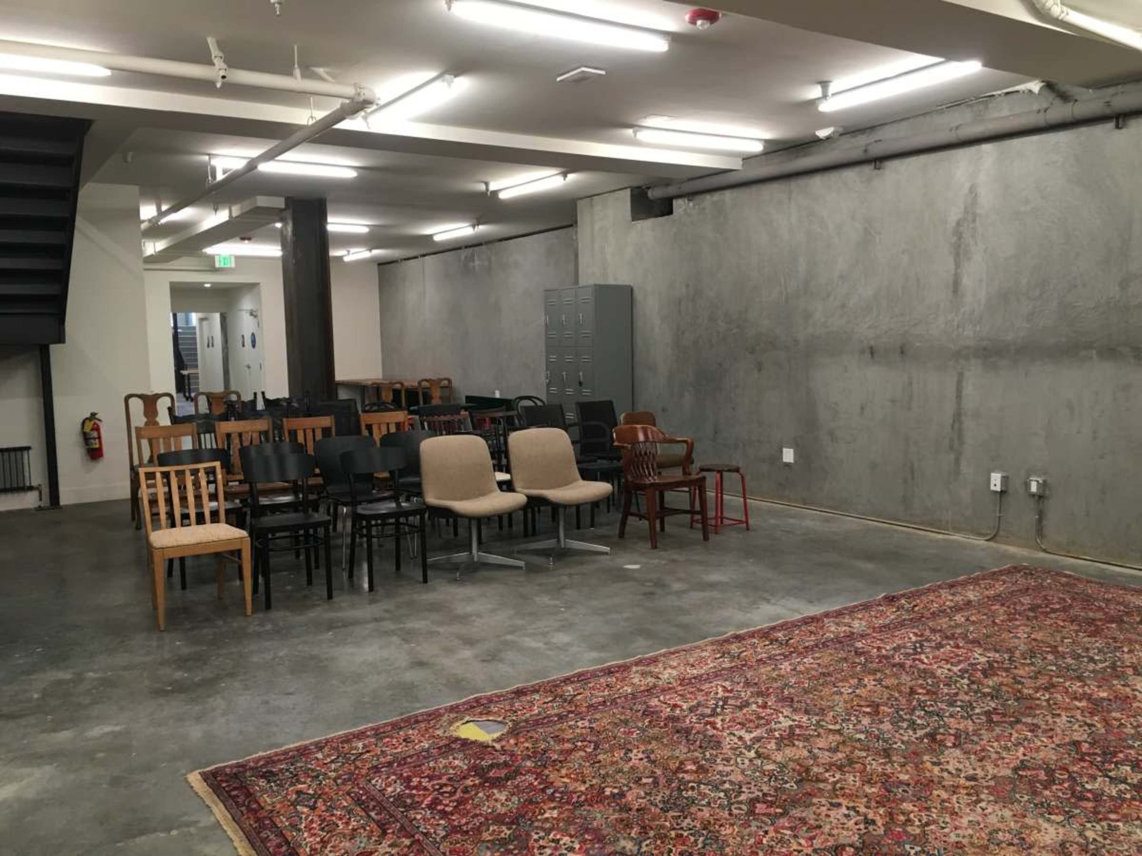 The image shows a room with a variety of chairs arranged in rows, a gray wall, a carpet on the floor, and lockers in the background.