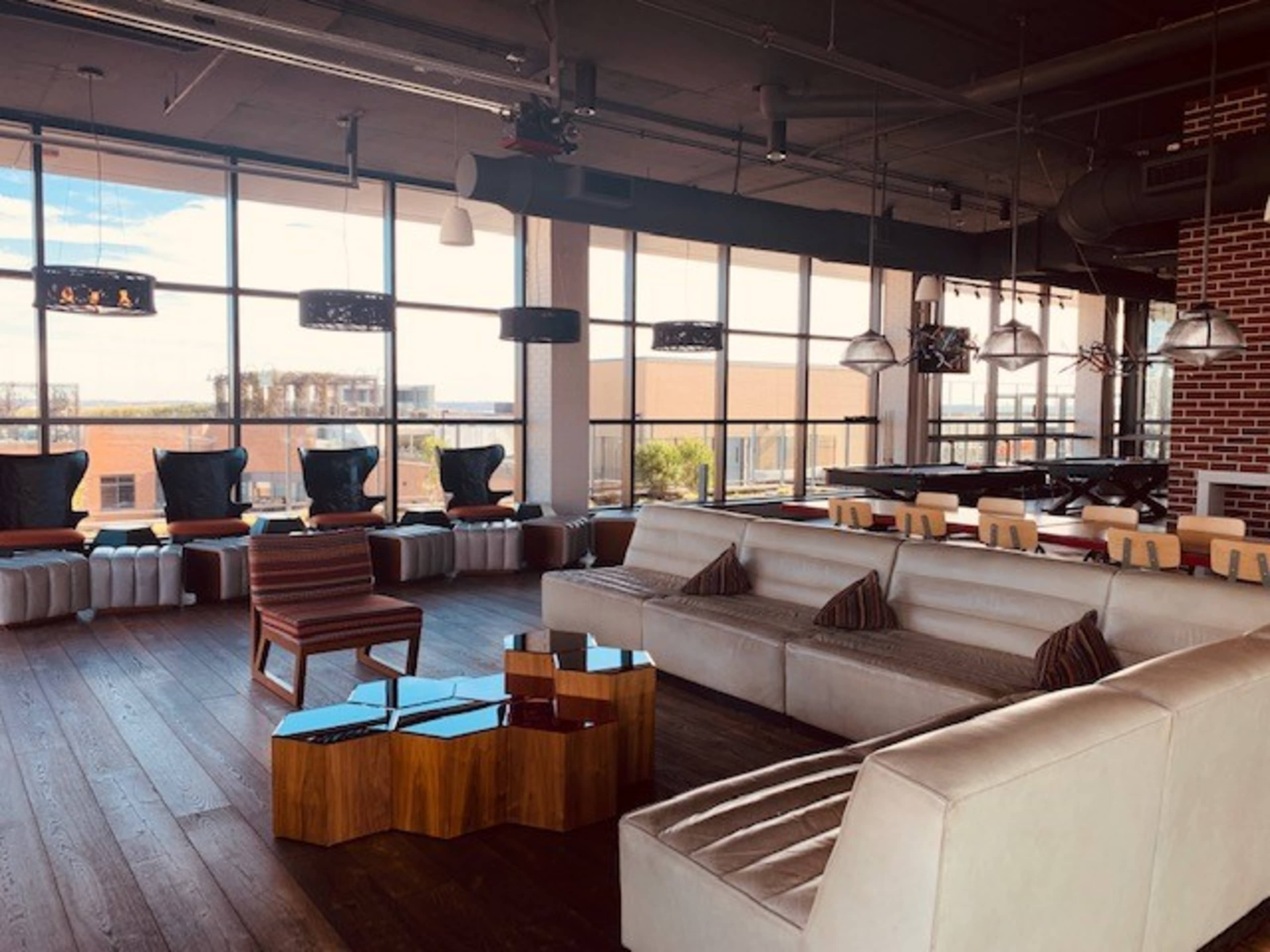 A modern lounge area with large windows, comfortable seating, and stylish wooden tables.