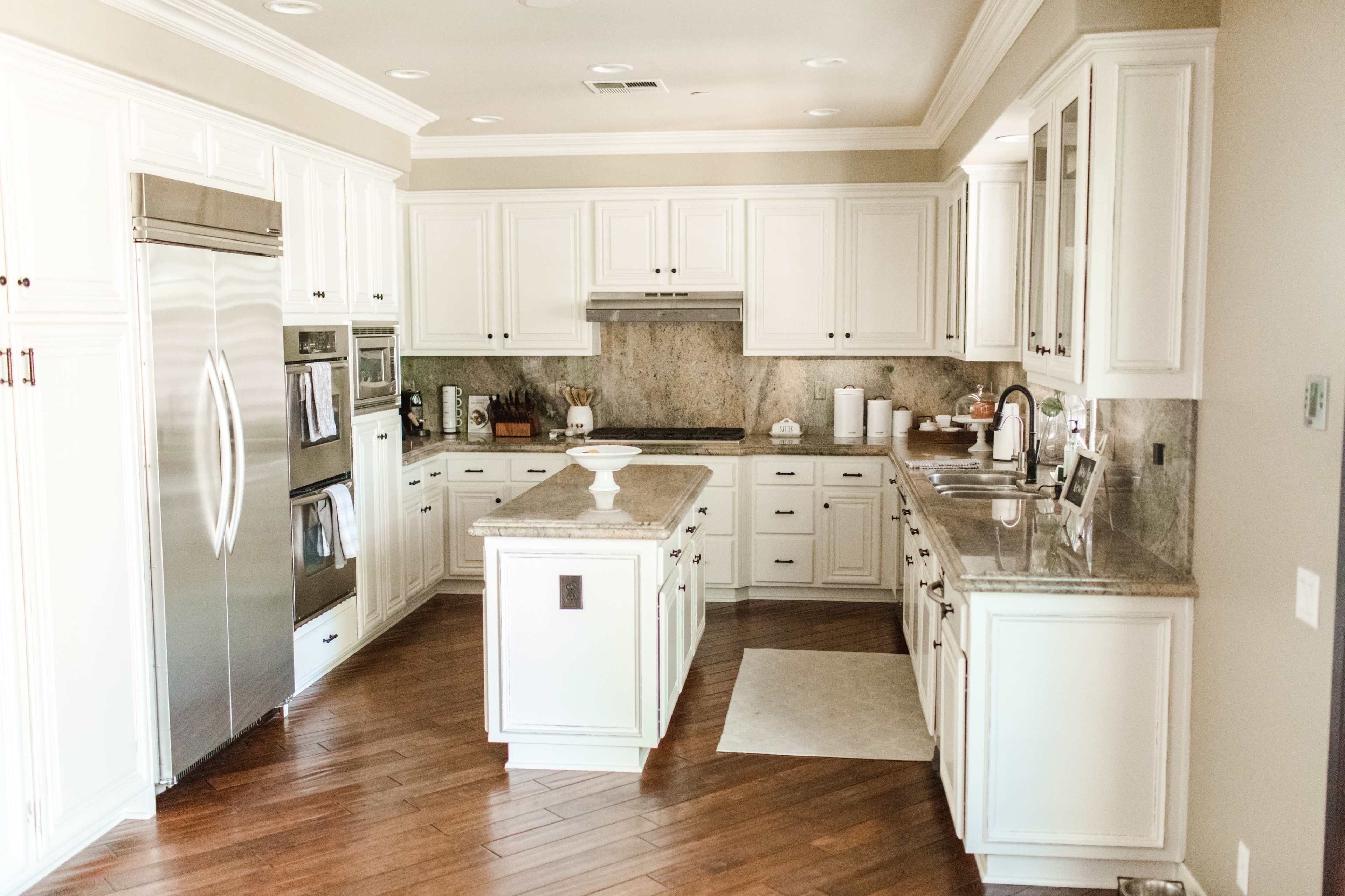 The image shows a modern kitchen with white cabinetry, stainless steel appliances, and a central island.