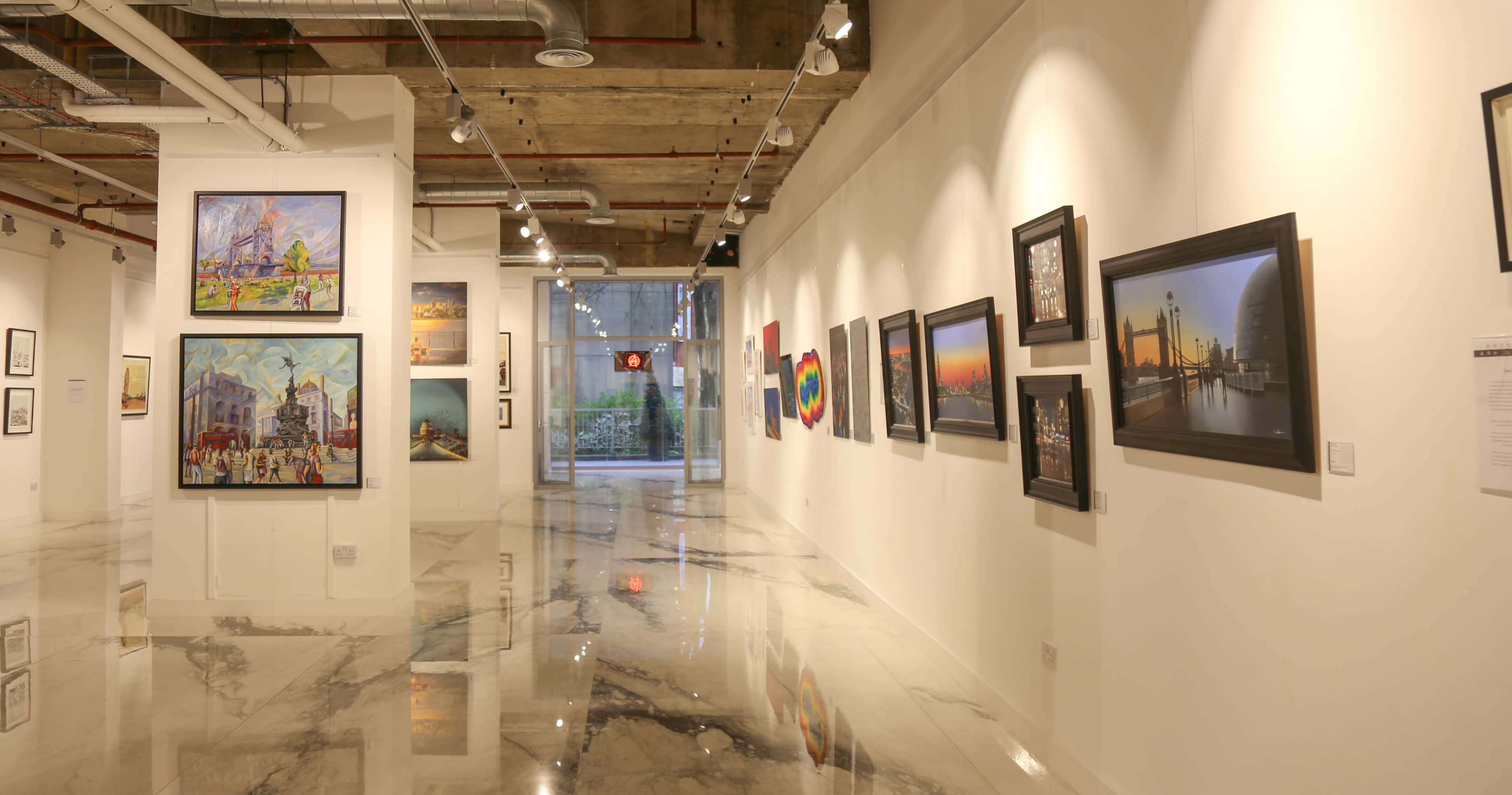The image shows a modern art gallery with multiple framed paintings displayed along white walls and a polished marble floor.