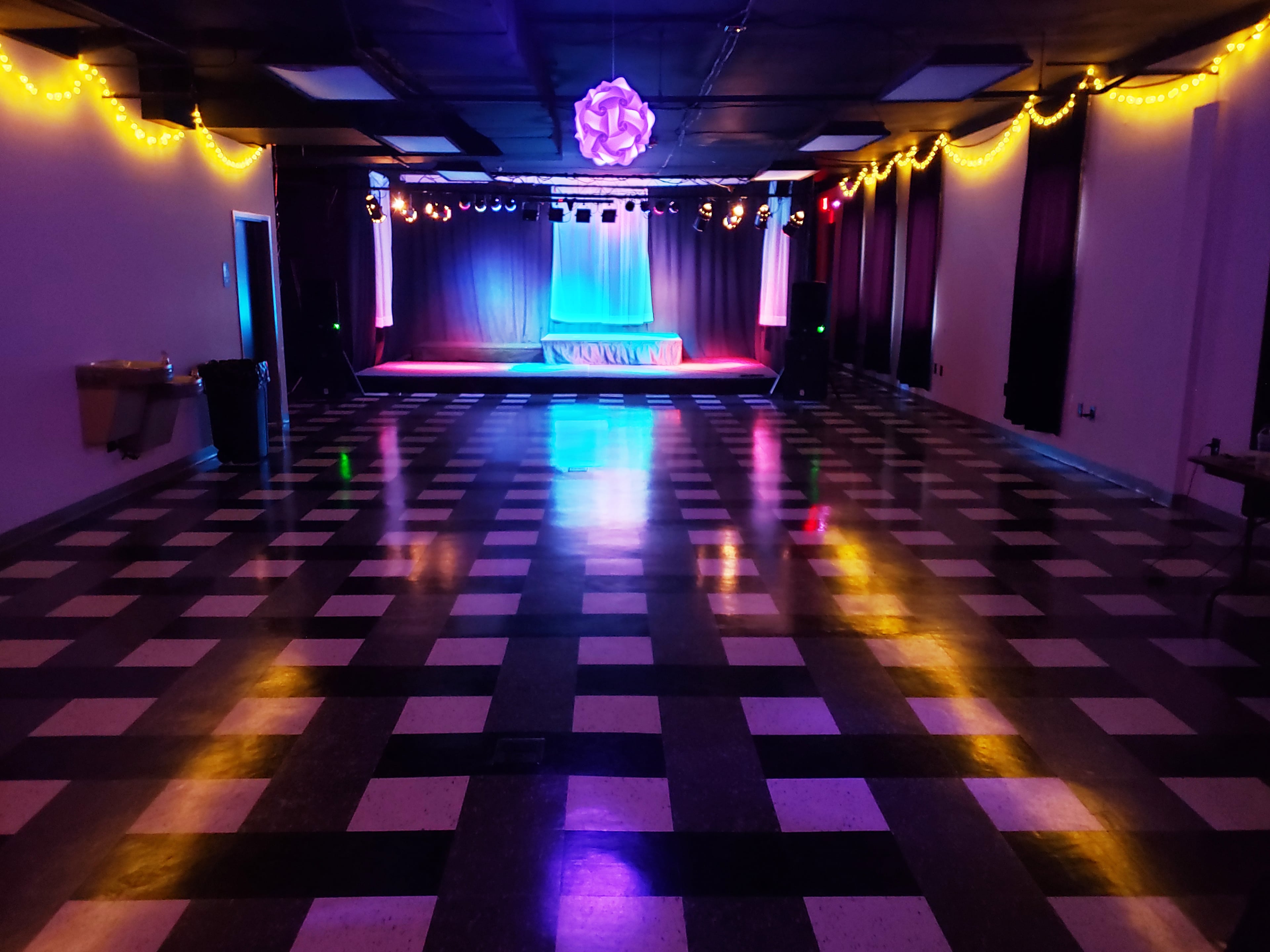 An empty dance hall with a checkered floor, stage lighting, and decorations along the ceiling.