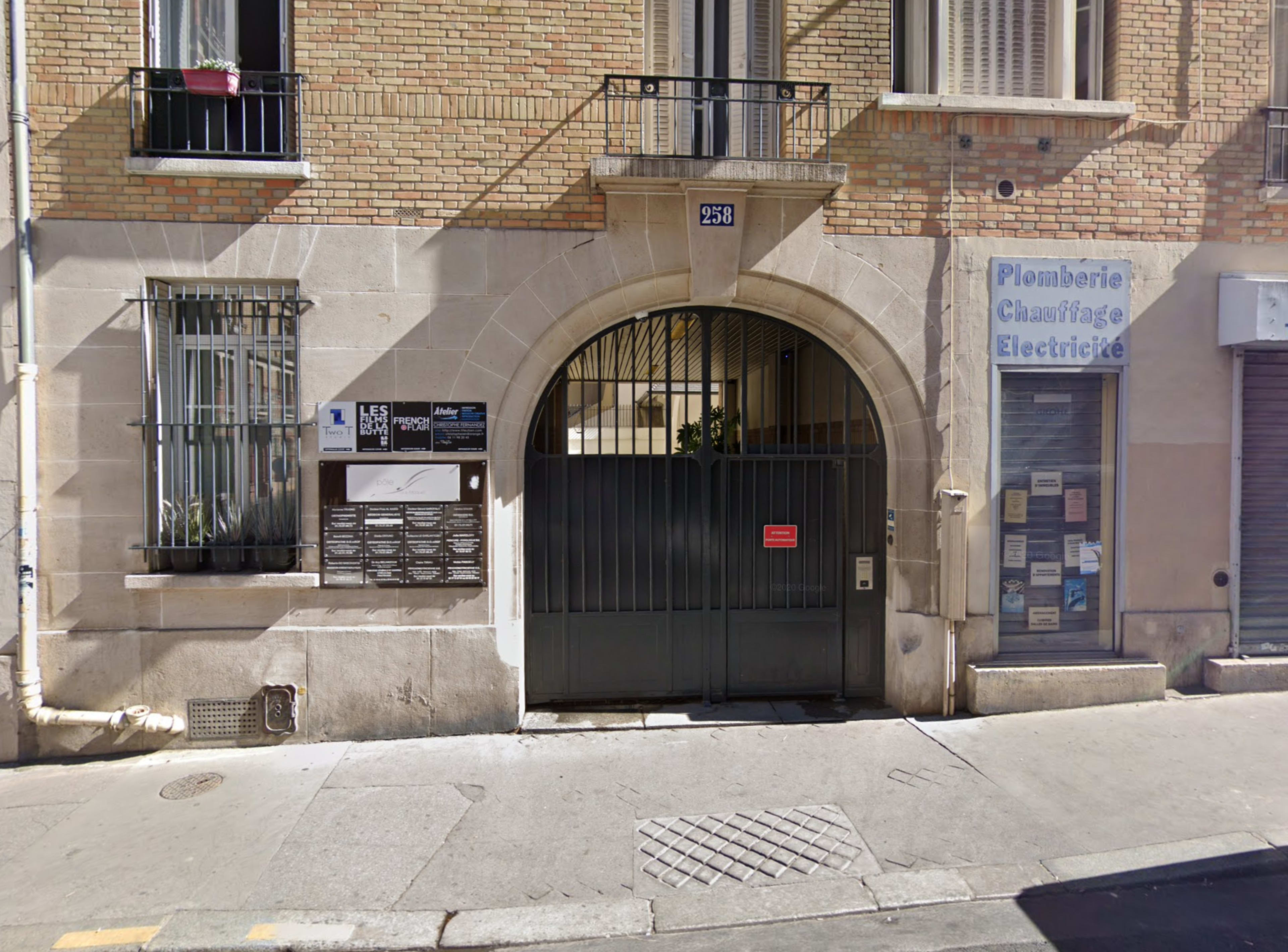A stone archway entrance with a barred gate, leading to a building facade featuring signage for plumbing and electrical services.