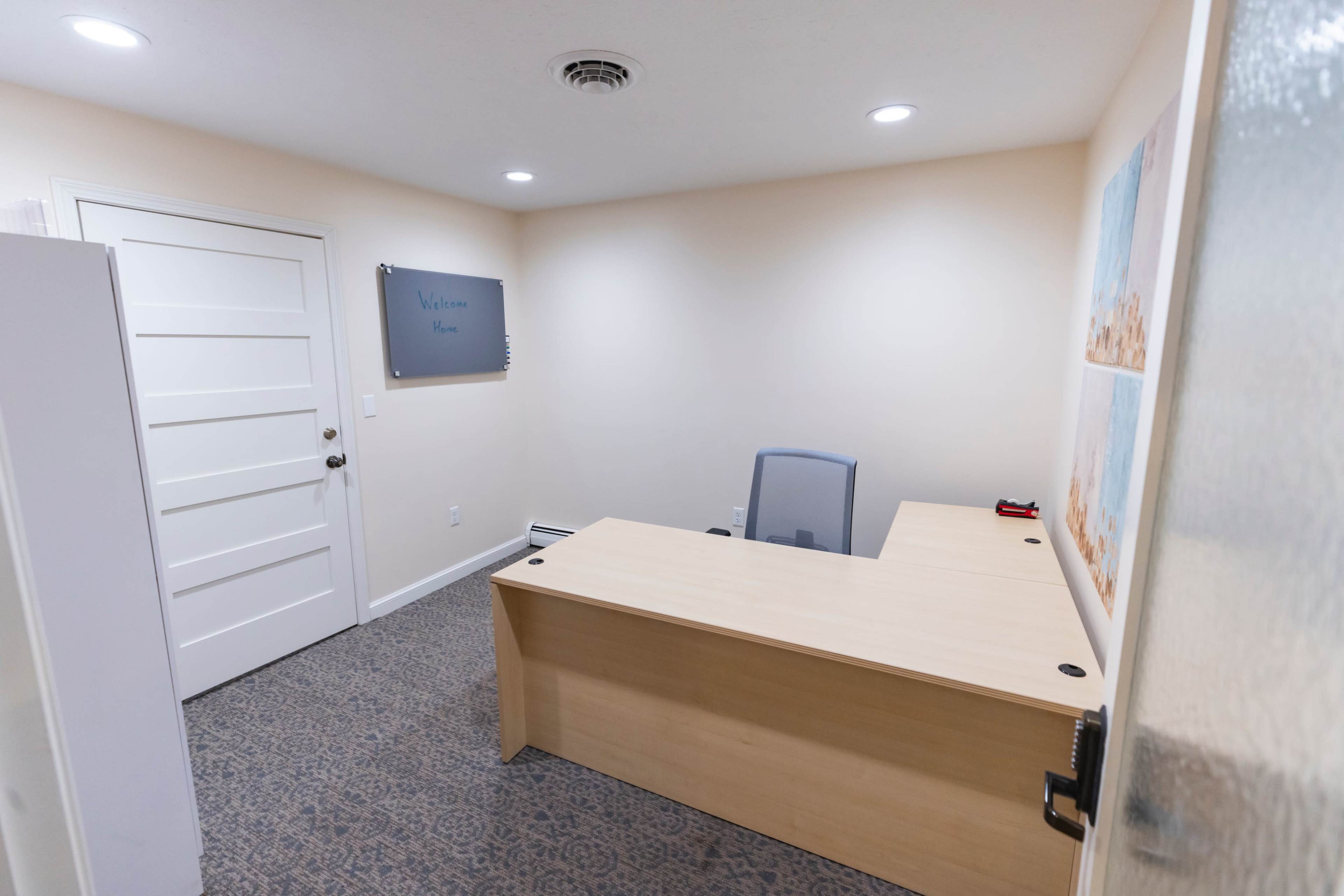 A small, empty office with a desk, a chair, and a welcoming sign on the wall.