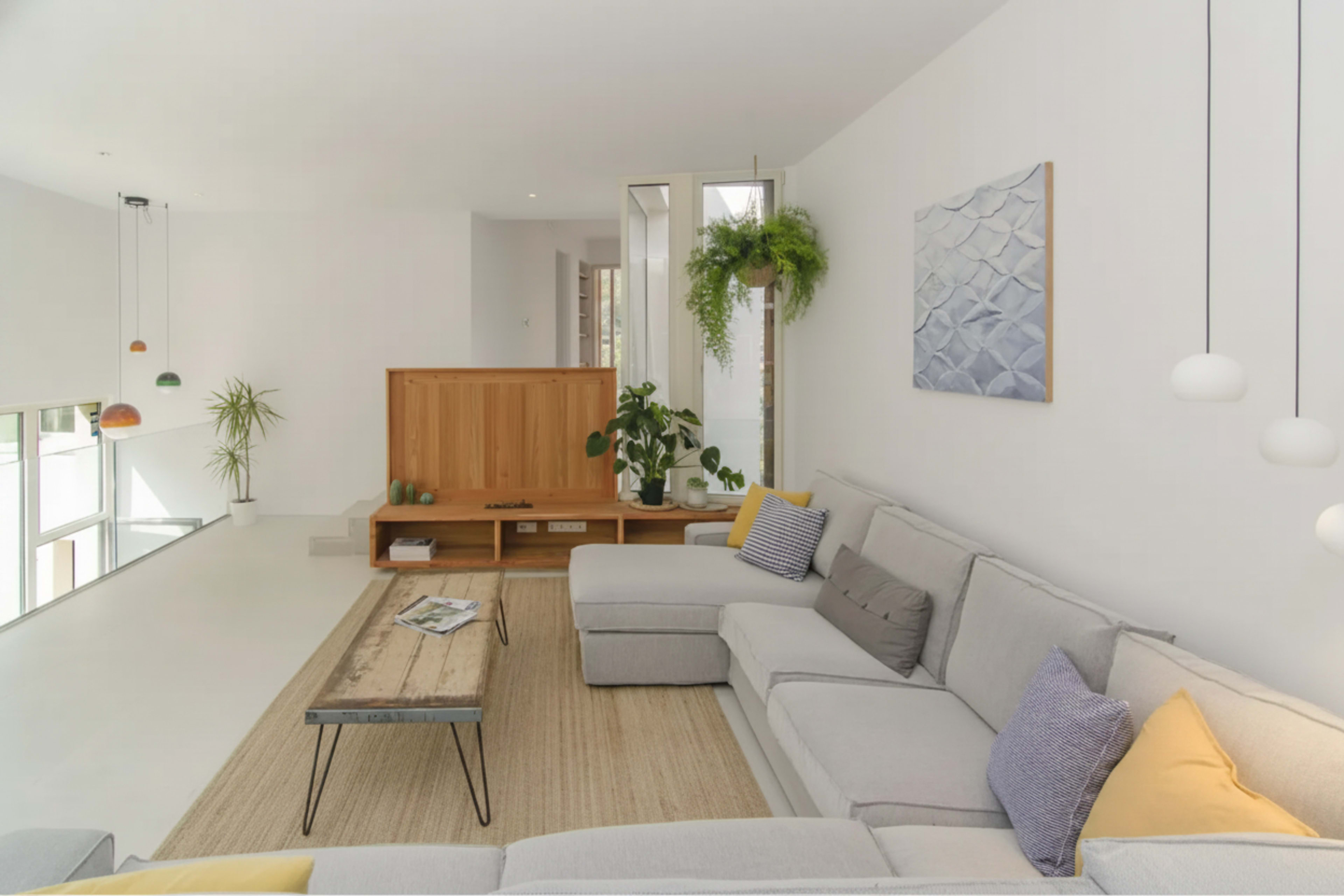 The image shows a modern living room with a gray sectional sofa, a wooden coffee table, and a minimalist design featuring plants and decorative art on the walls.